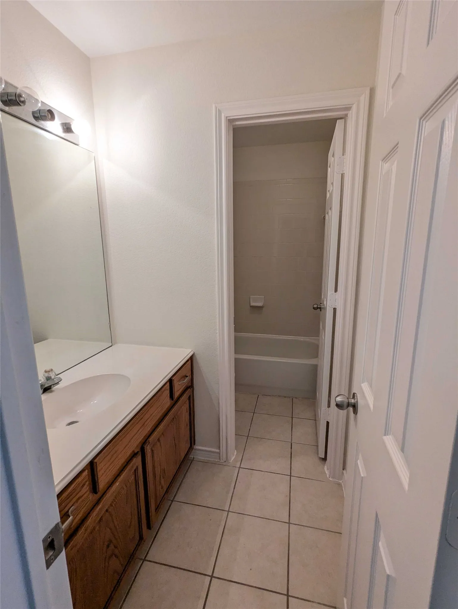 Bathroom featuring a single vanity with a white countertop, wood-finish cabinetry, a large mirror, and tiled flooring