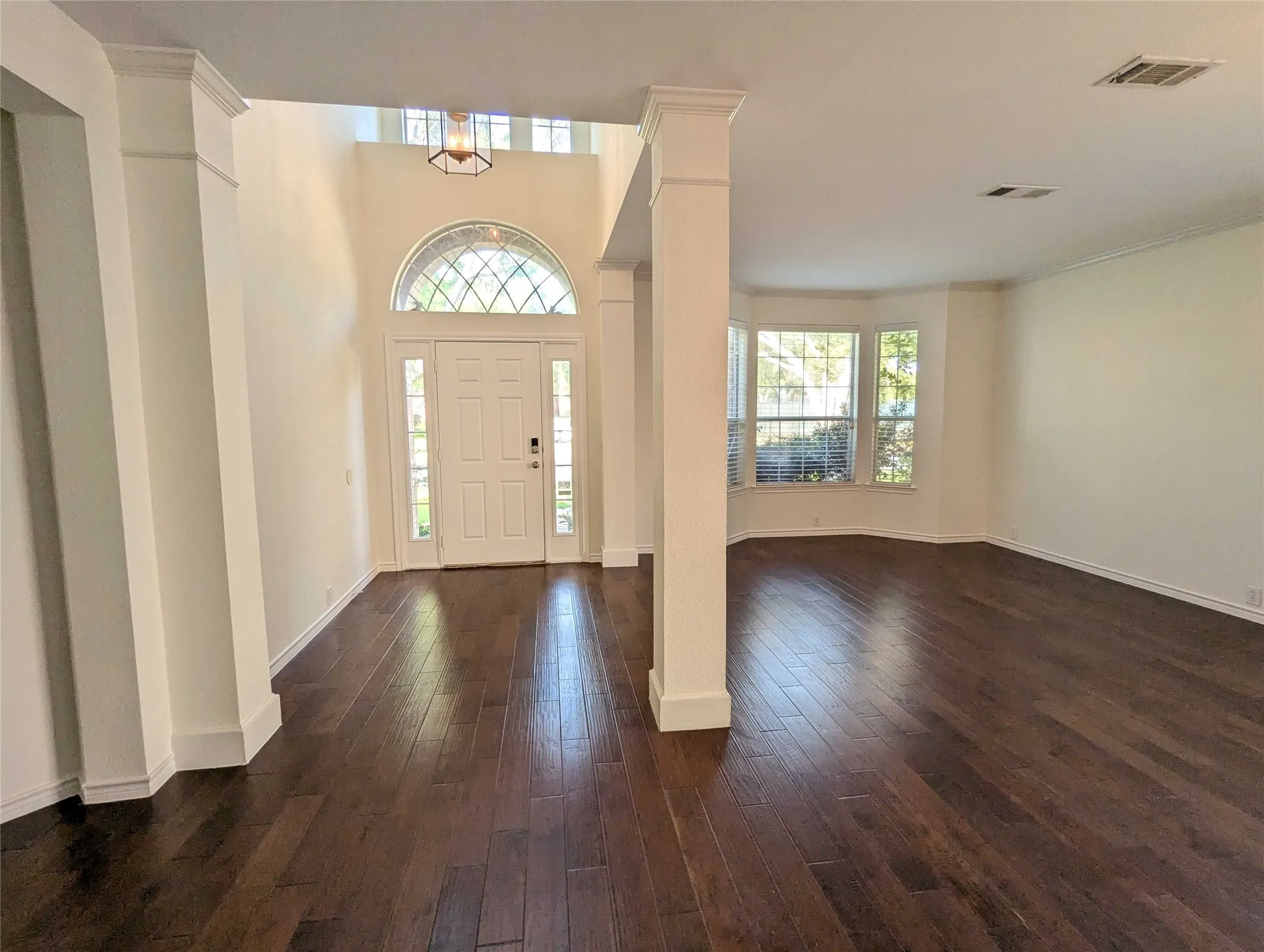 Expansive wood-finish flooring throughout, featuring a prominent entry door with sidelights and an arched transom window