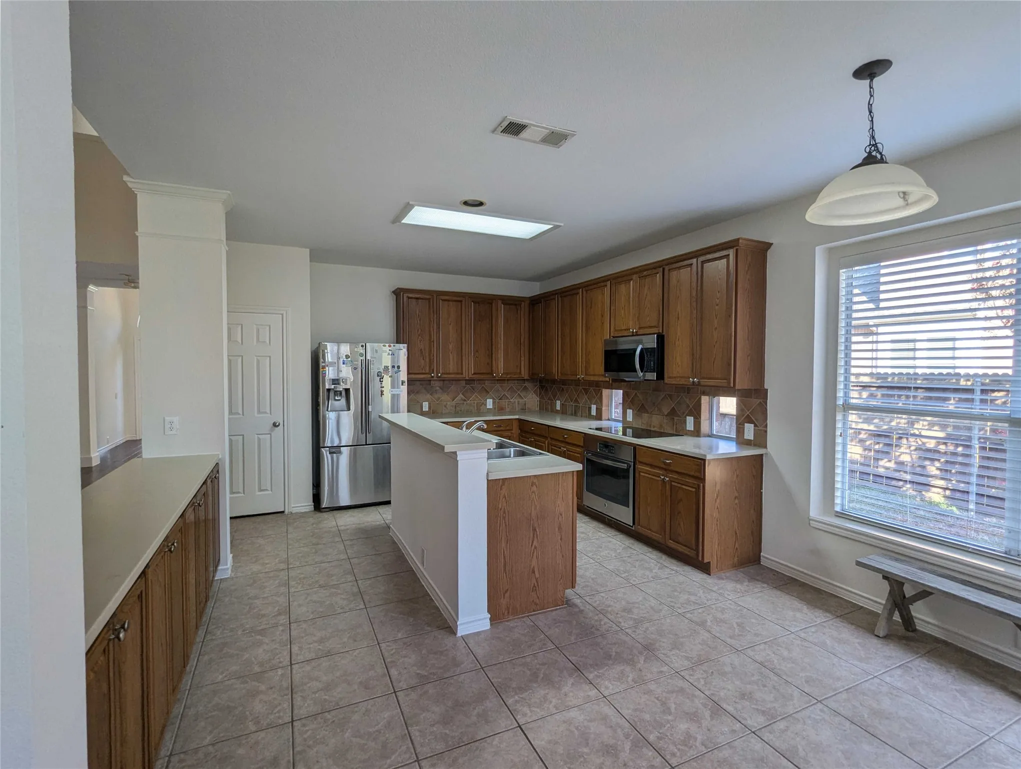 Kitchen featuring wood cabinetry, tile flooring, recessed lighting, a skylight, and stainless steel appliances