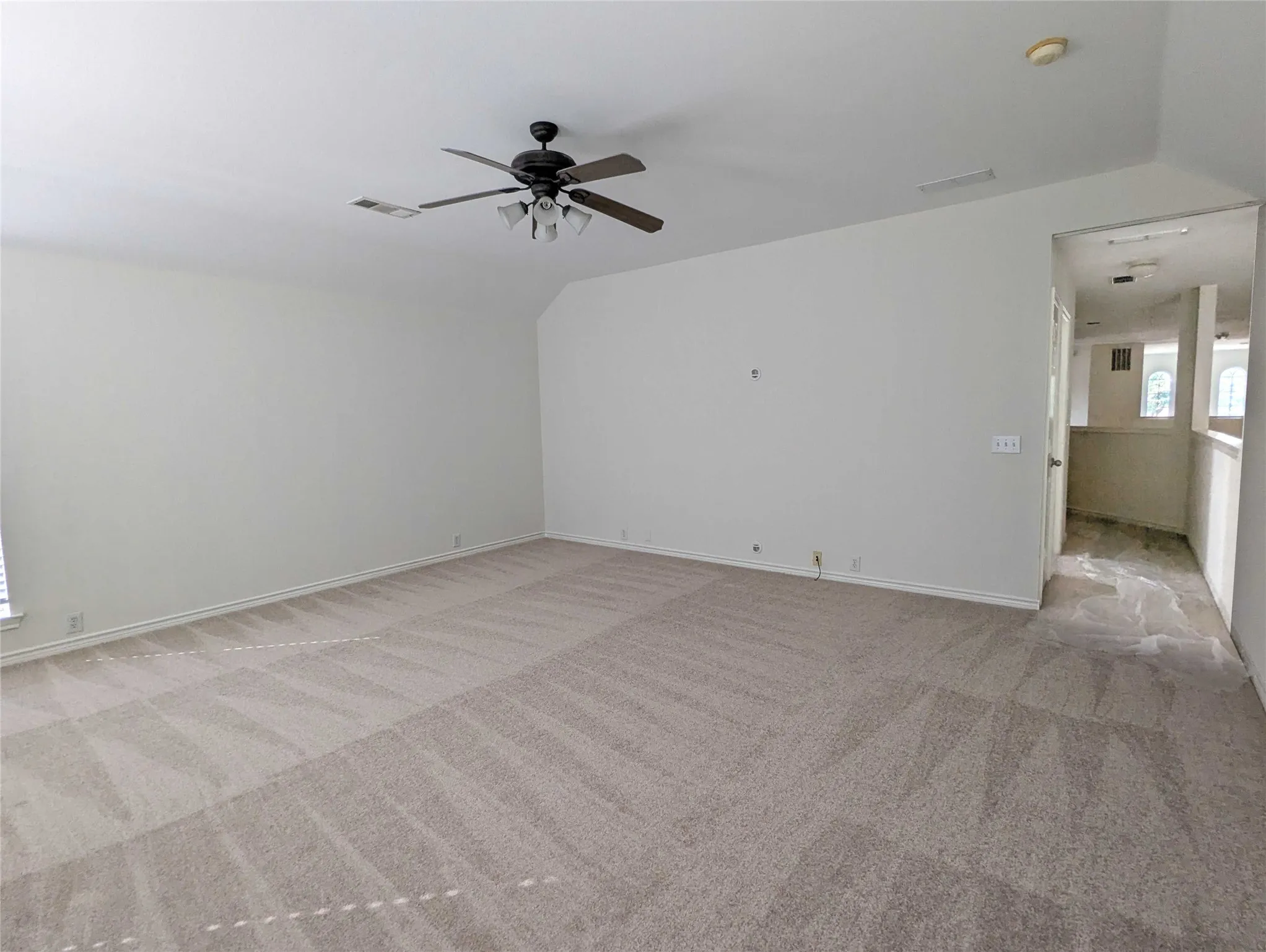 Expansive carpeted room featuring a ceiling fan with integrated lighting and neutral wall tones