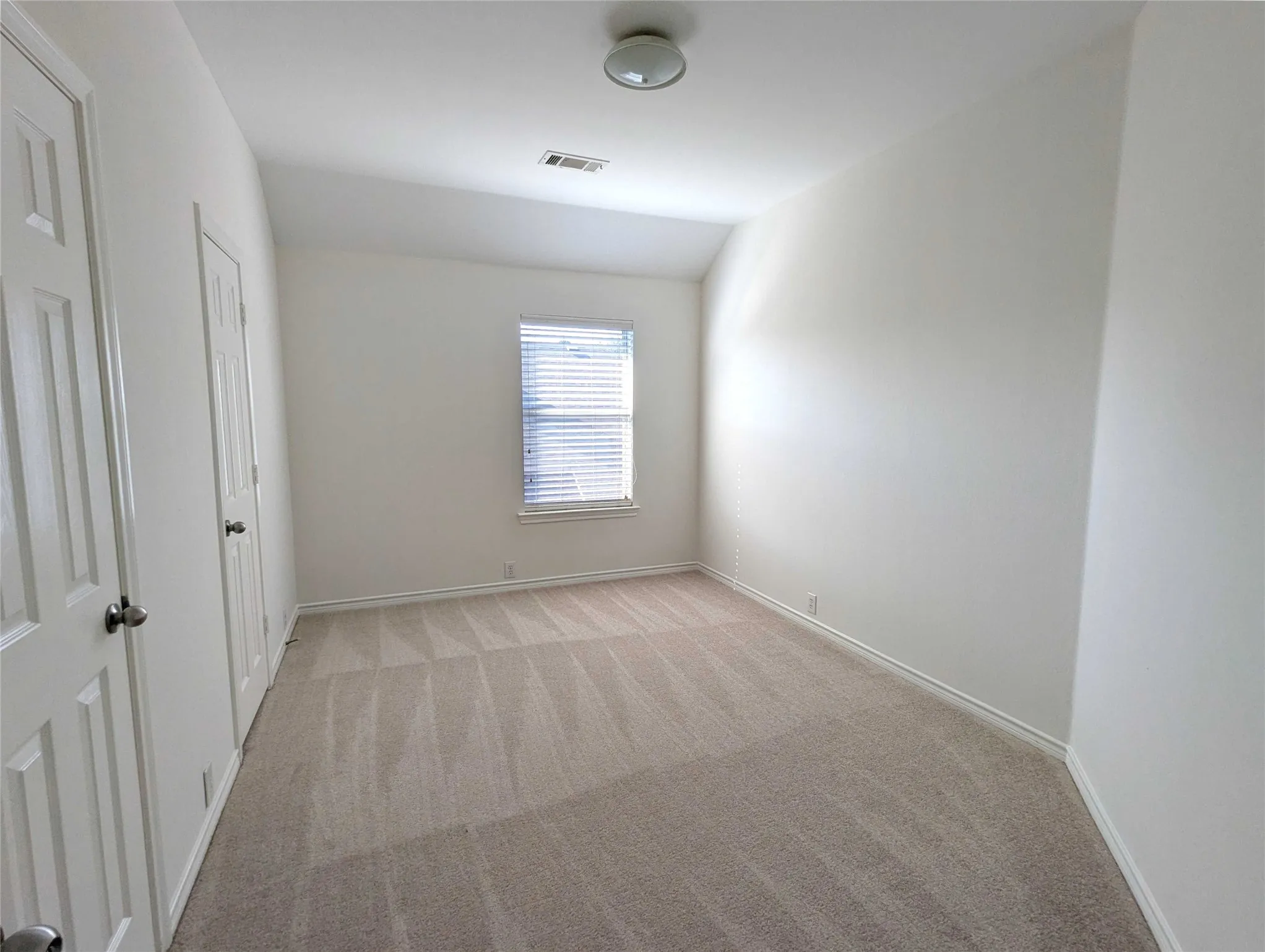Neutral tone wall paint, carpet flooring, window with horizontal blinds, overhead light fixture, and paneled doors