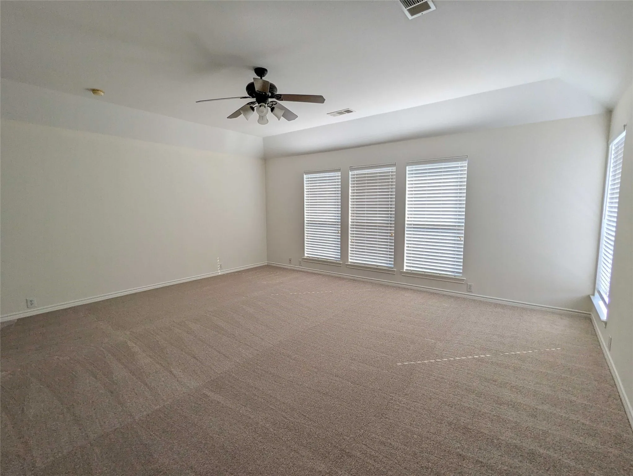 Recessed ceiling with a central ceiling fan, multiple windows with blinds, and neutral carpeting