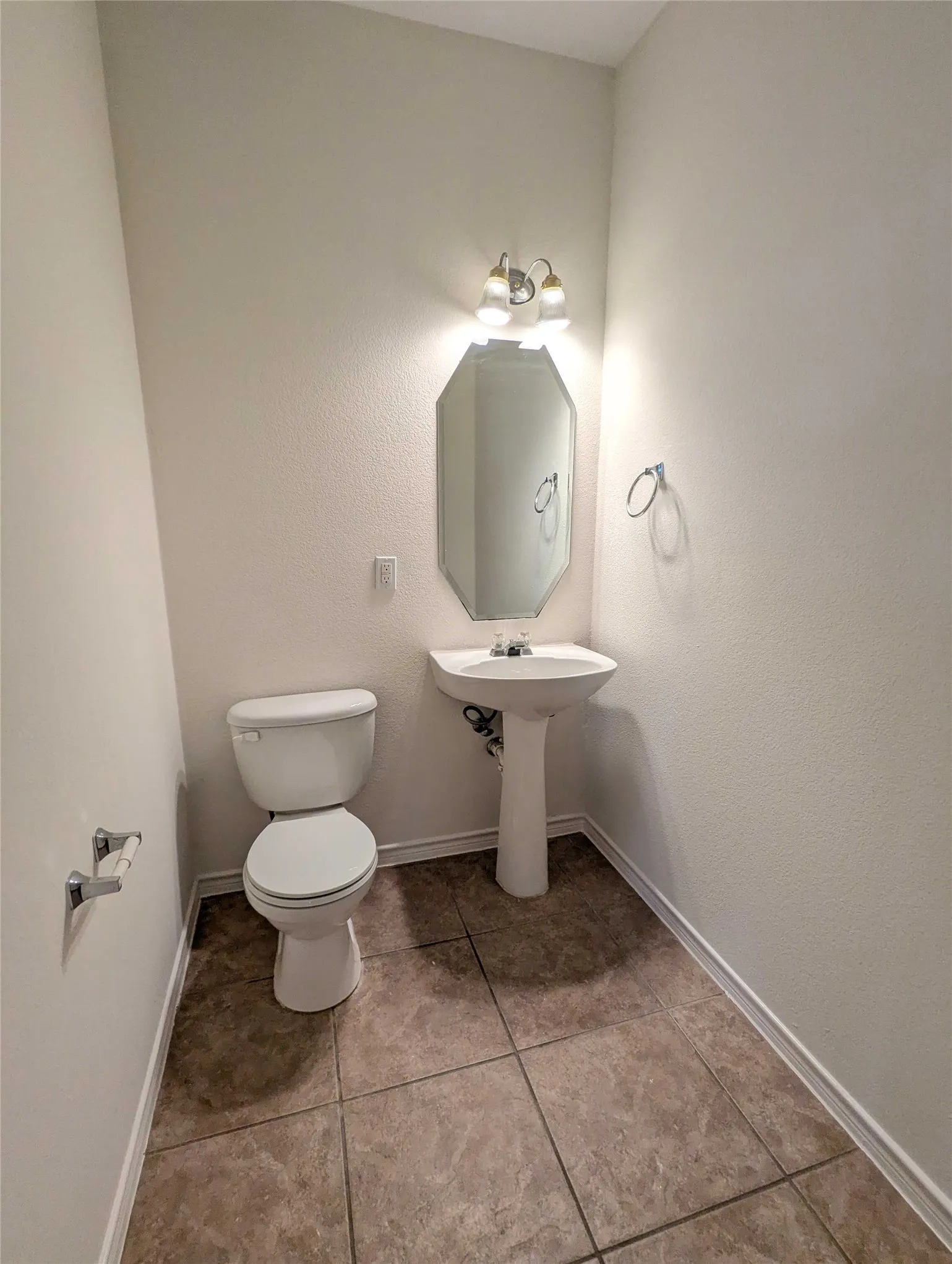 Pedestal sink with a white ceramic toilet, tile flooring, and wall-mounted vanity lighting