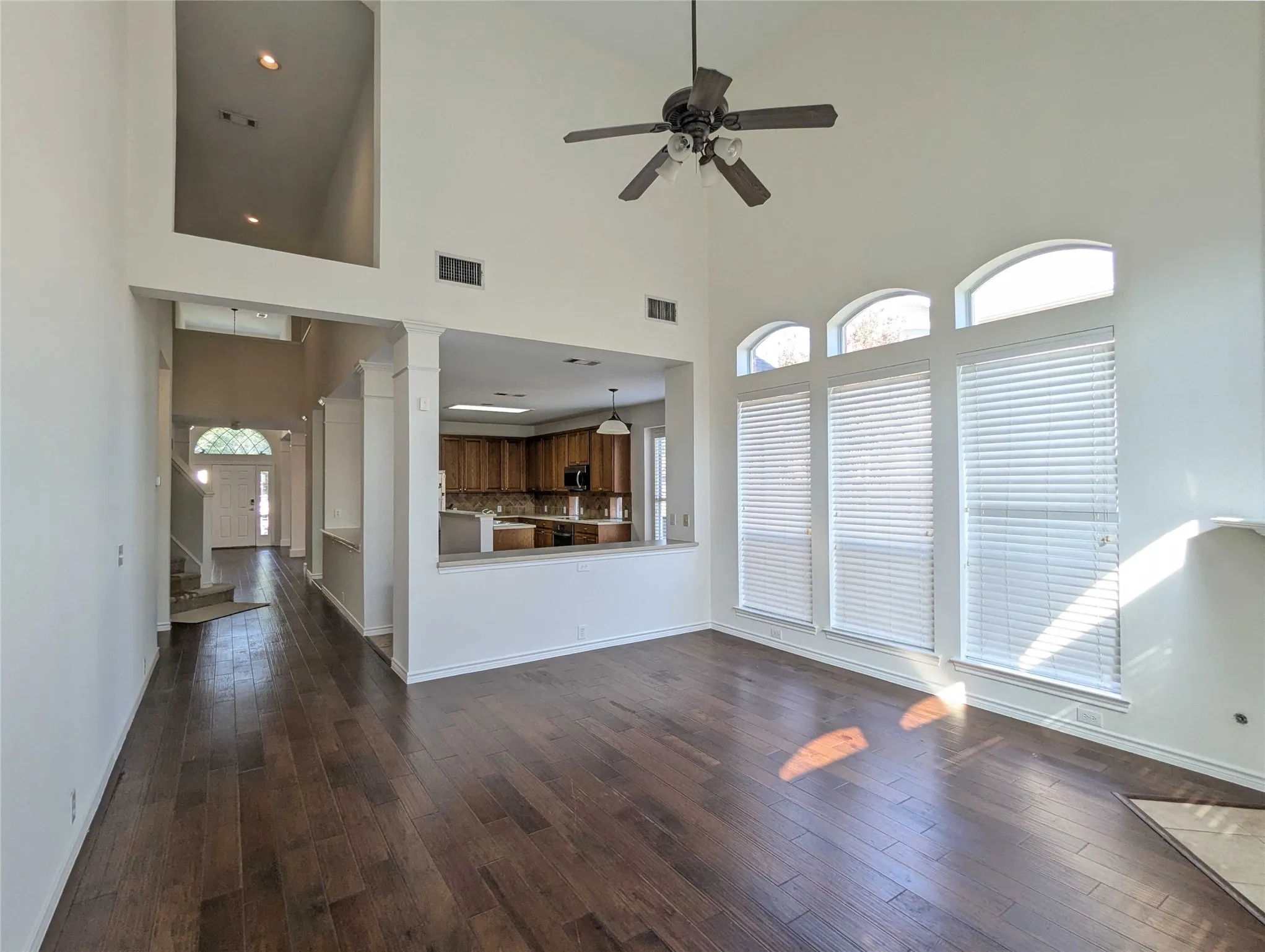Soaring ceilings with integrated lighting, wood-finish flooring, a ceiling fan, and multiple arched windows with blinds