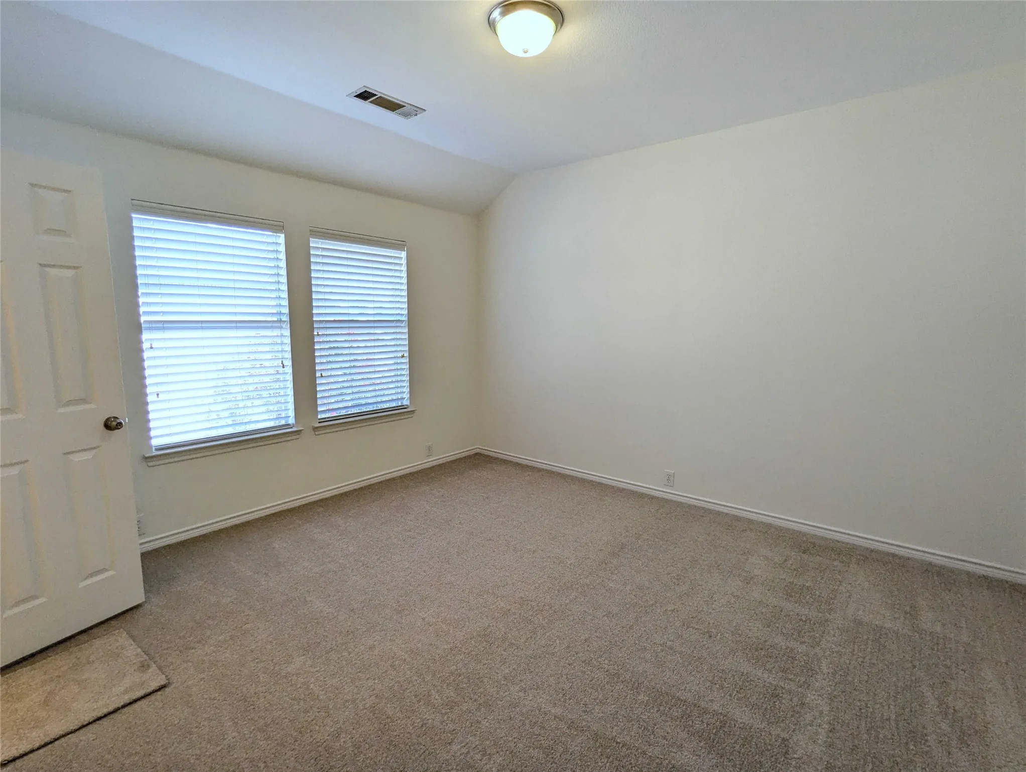 Neutral wall tones, dual windows with horizontal blinds, overhead flush mount lighting, and carpeted flooring