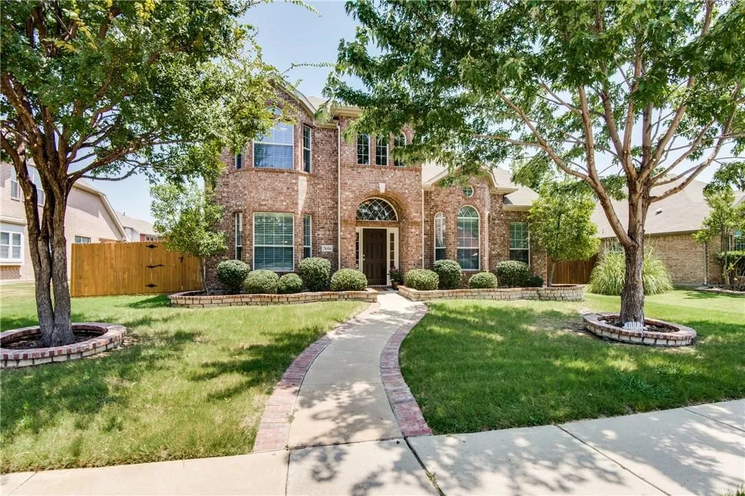 Brick facade residence with arched entry, mature trees, and landscaped shrubbery