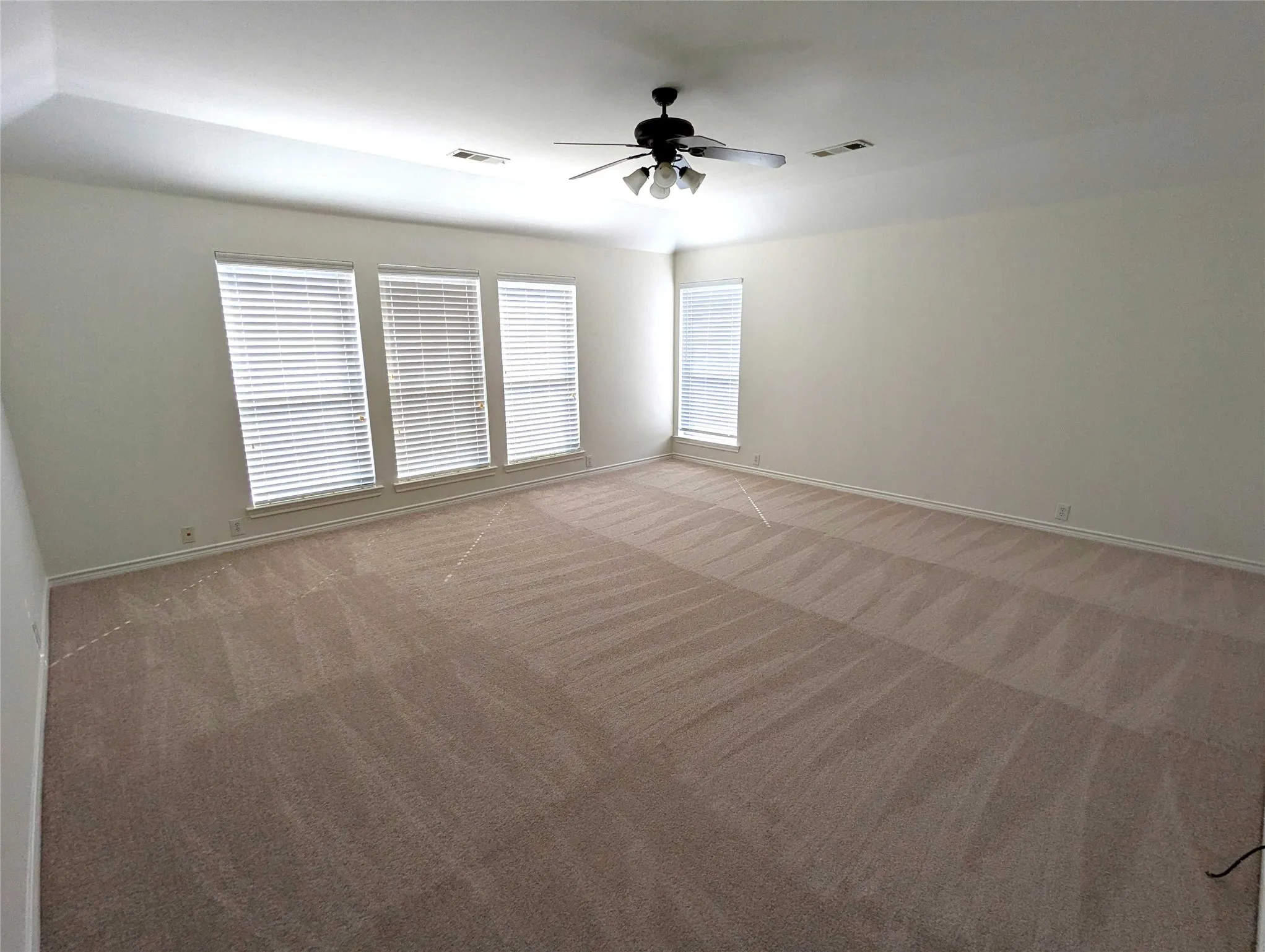 Spacious room with plush carpeting, multiple windows with blinds, recessed lighting, and a ceiling fan