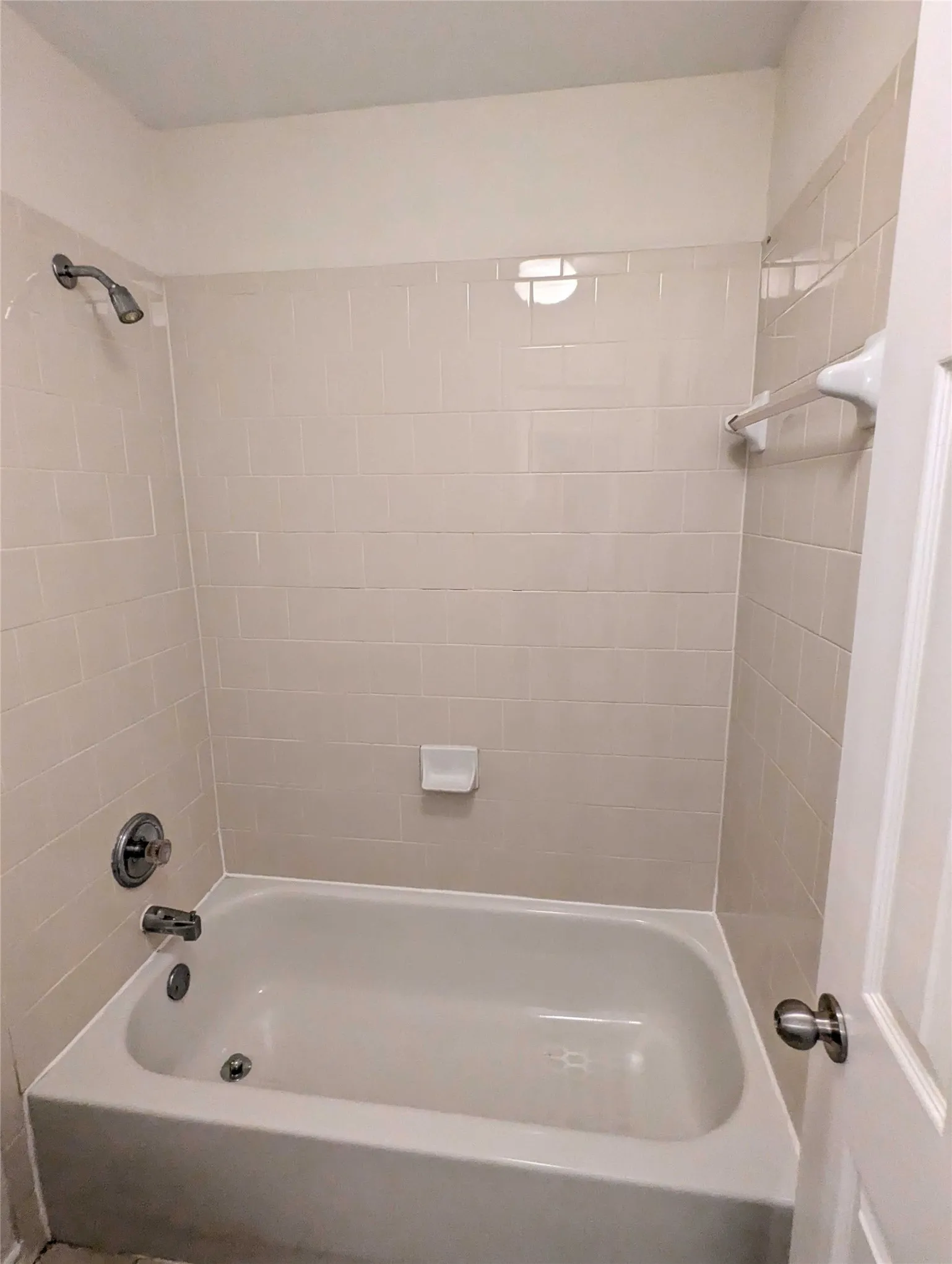 Enclosed bathtub with a shower fixture, wall-mounted soap dish, and a white tile surround