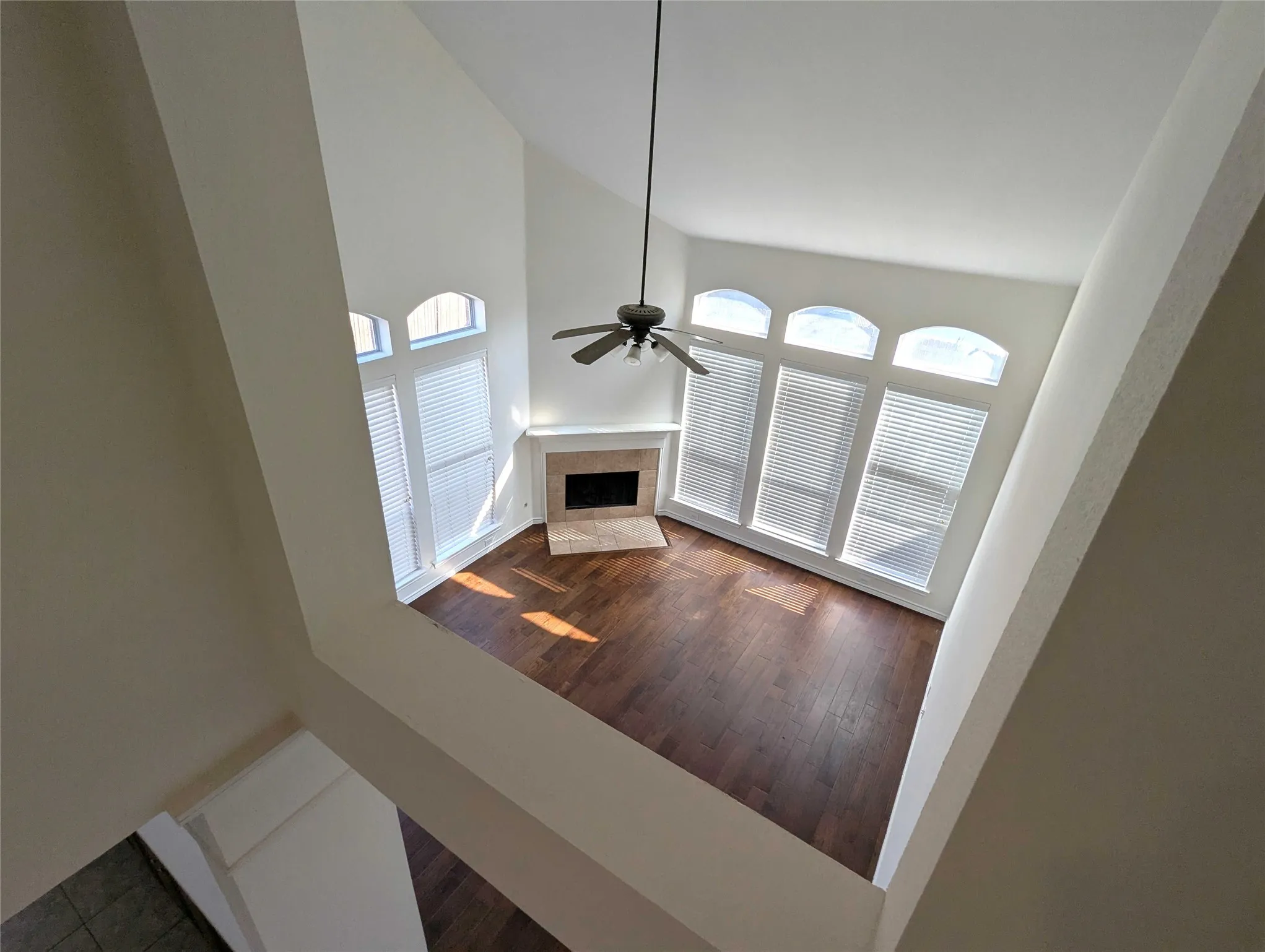 Vaulted ceiling with a ceiling fan, arched windows with blinds, built-in fireplace, and wood-finish flooring
