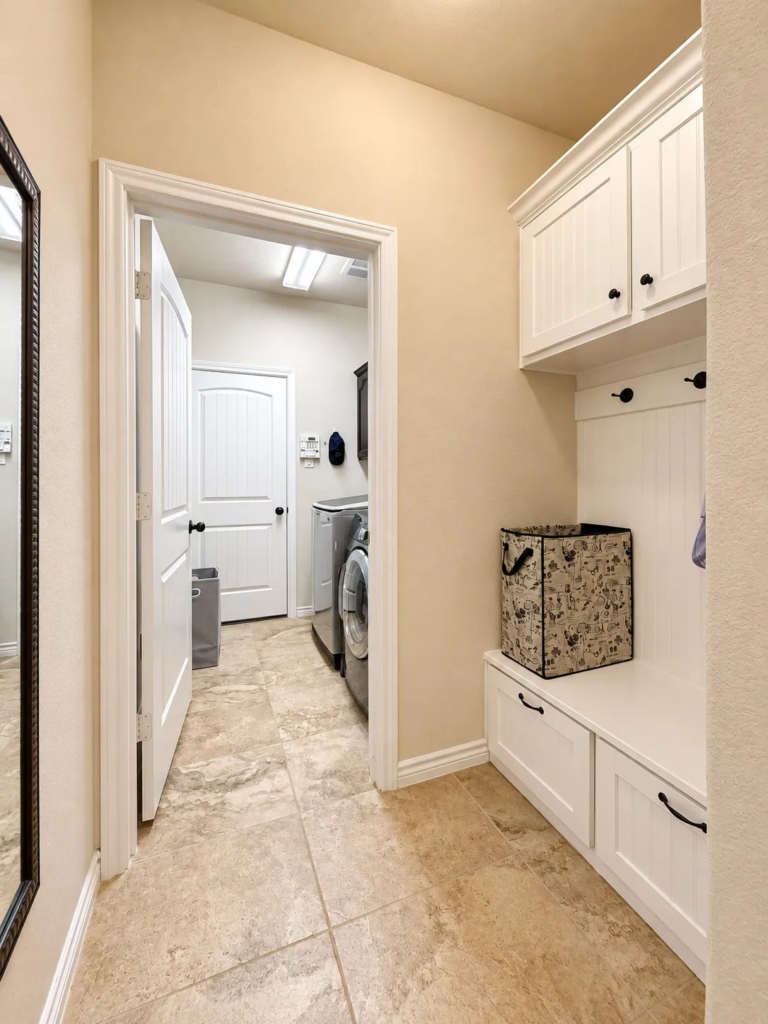 Built-in white cabinetry with black hardware, integrated bench seating, wall-mounted hooks, and neutral tile flooring