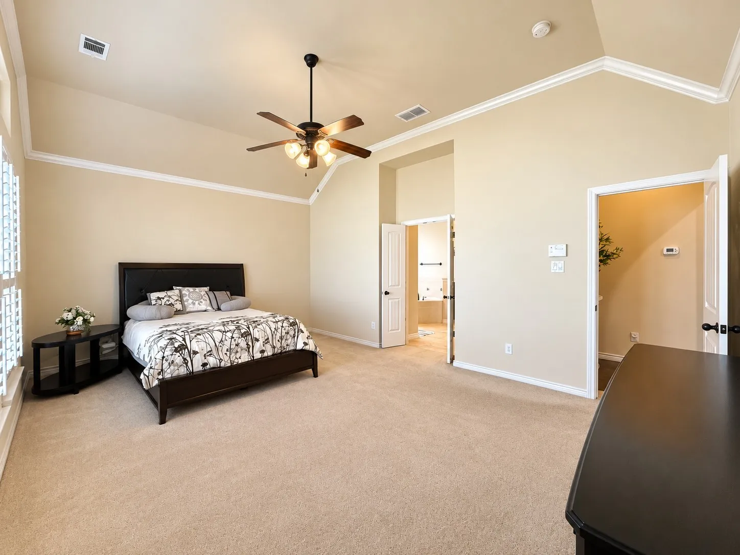 Spacious primary bedroom suite featuring a ceiling fan with integrated lighting, neutral carpeting throughout, and abundant natural light from multiple windows