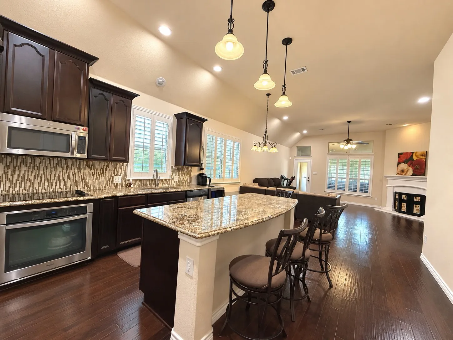 Kitchen featuring dark wood cabinetry, granite countertops, stainless steel appliances, and a mosaic tile backsplash