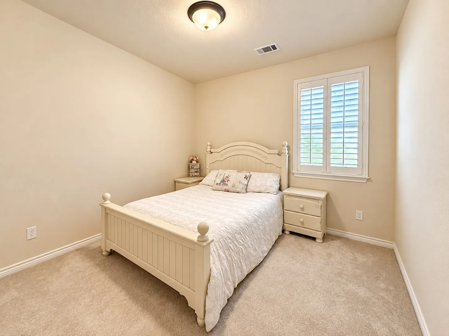 Bright secondary bedroom featuring neutral wall finishes, carpet flooring, and a large window with plantation shutters providing natural light and privacy