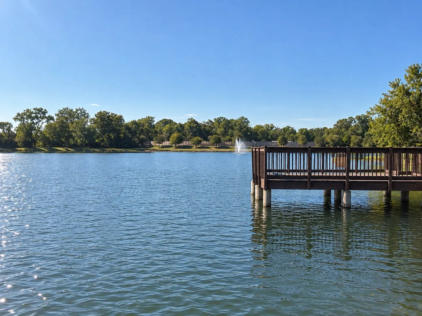 Wood-finish pier with railing extending over water, surrounded by mature trees