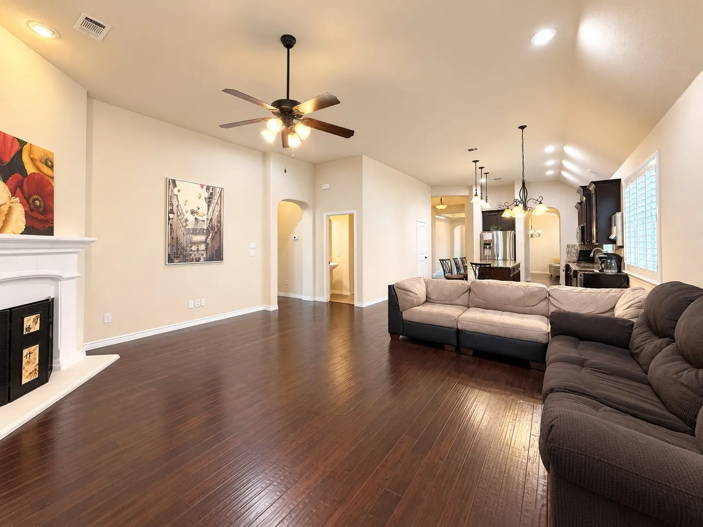 Spacious interior with dark wood-finish flooring, a white mantel fireplace, and a ceiling fan with integrated lighting