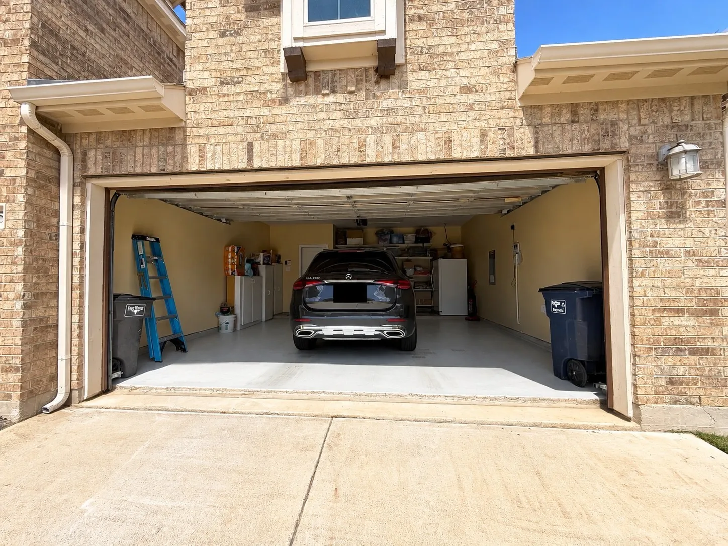 Attached garage with a light-colored brick exterior, a concrete driveway, and an exterior wall light fixture