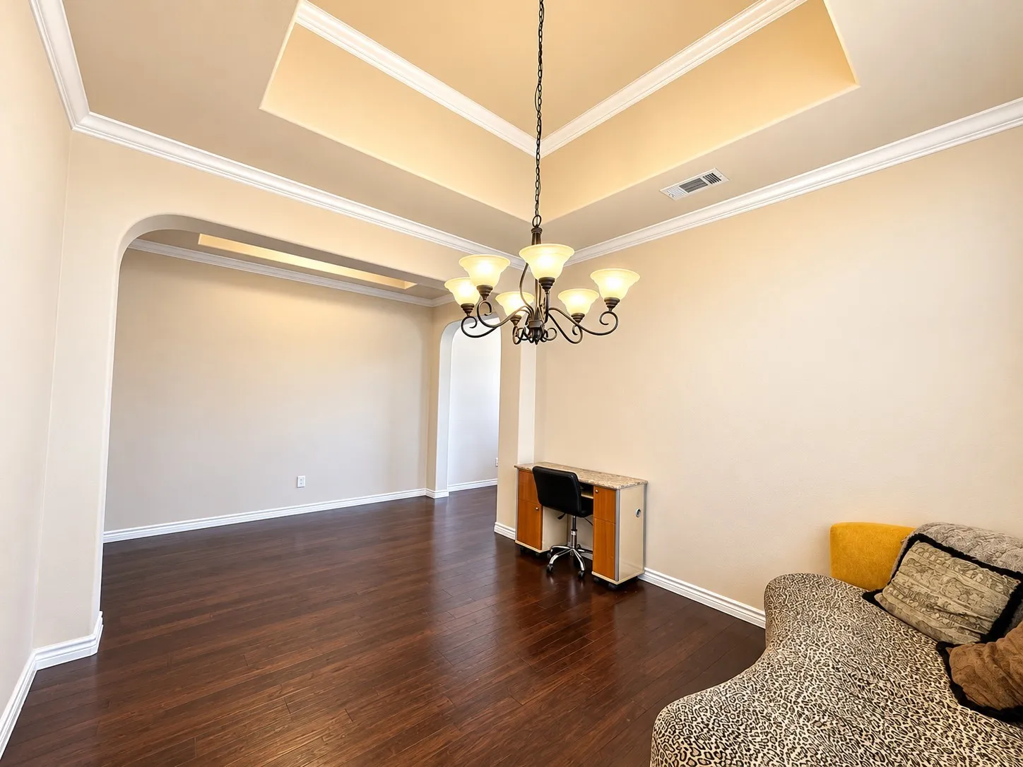 Recessed ceiling with layered crown molding, arched doorways, wood-finish flooring, and a decorative chandelier