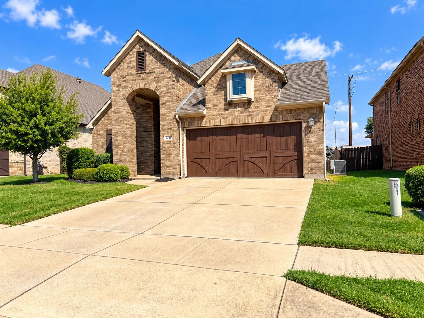 Brick exterior with an arched entryway, shingled roof, two-car garage, and concrete driveway