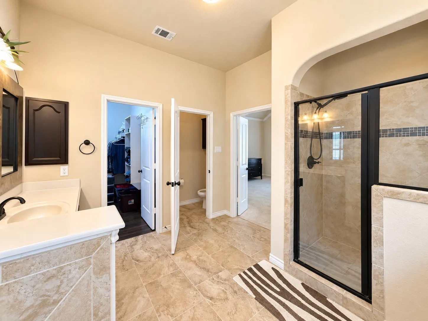 Walk-in shower with glass enclosure, single vanity with undermount sink, tiled flooring, and arched doorway