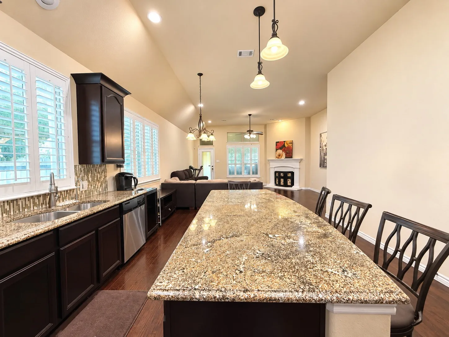 Kitchen island with granite countertop, dark wood-finish cabinetry, stainless steel dishwasher, and mosaic tile backsplash