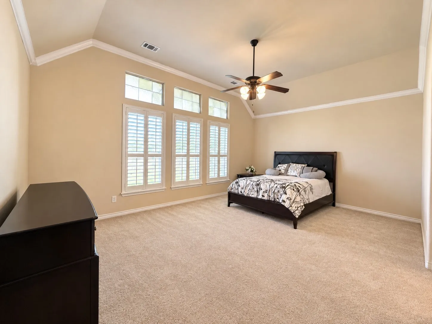 Vaulted ceiling with crown molding, ceiling fan, carpet flooring, and a wall of windows featuring plantation shutters