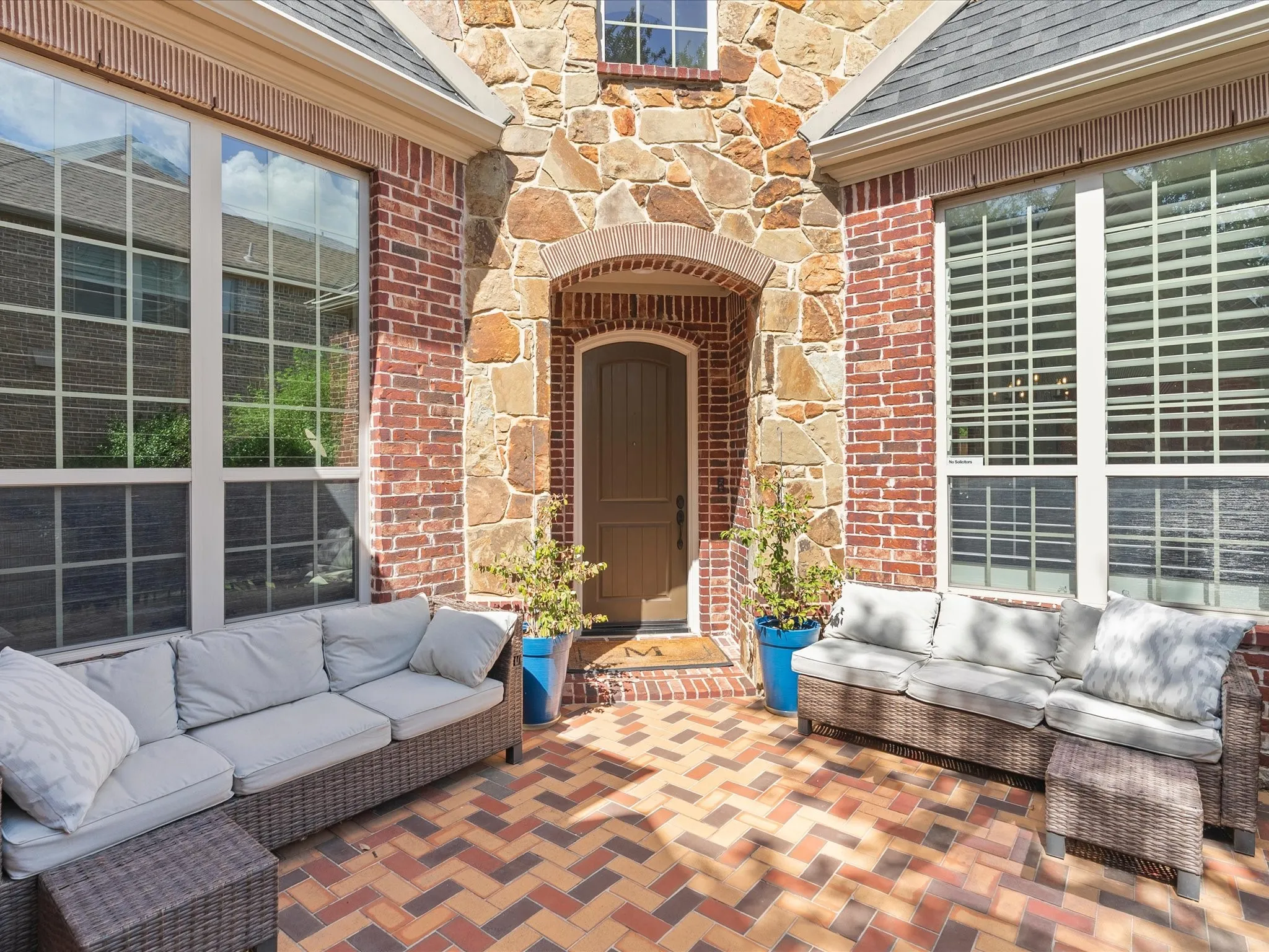 Brick and stone exterior with large pane windows, arched entryway, and a herringbone-patterned brick patio
