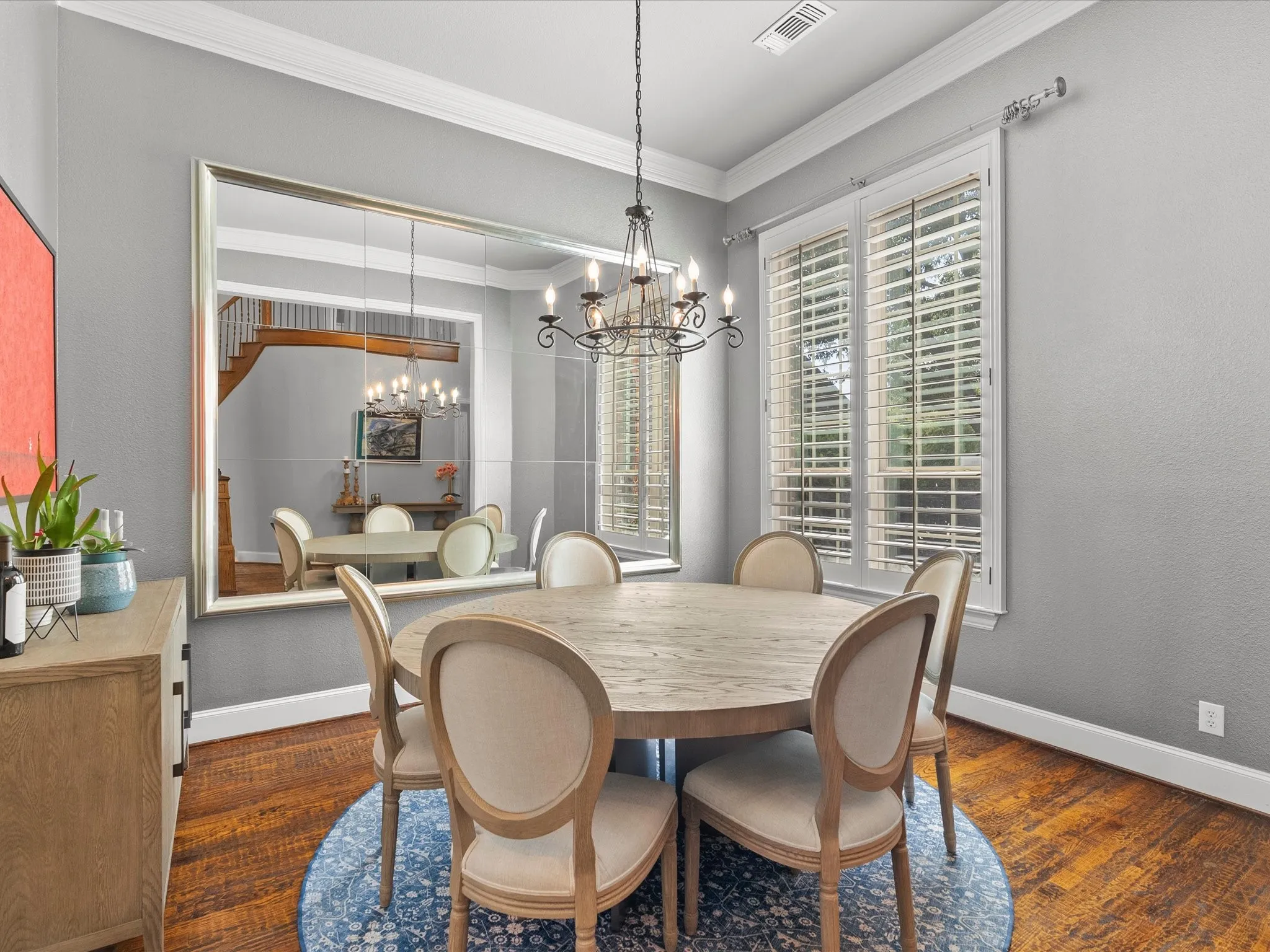 Hardwood flooring, crown molding, double windows with plantation shutters, and a chandelier with candelabra bulbs
