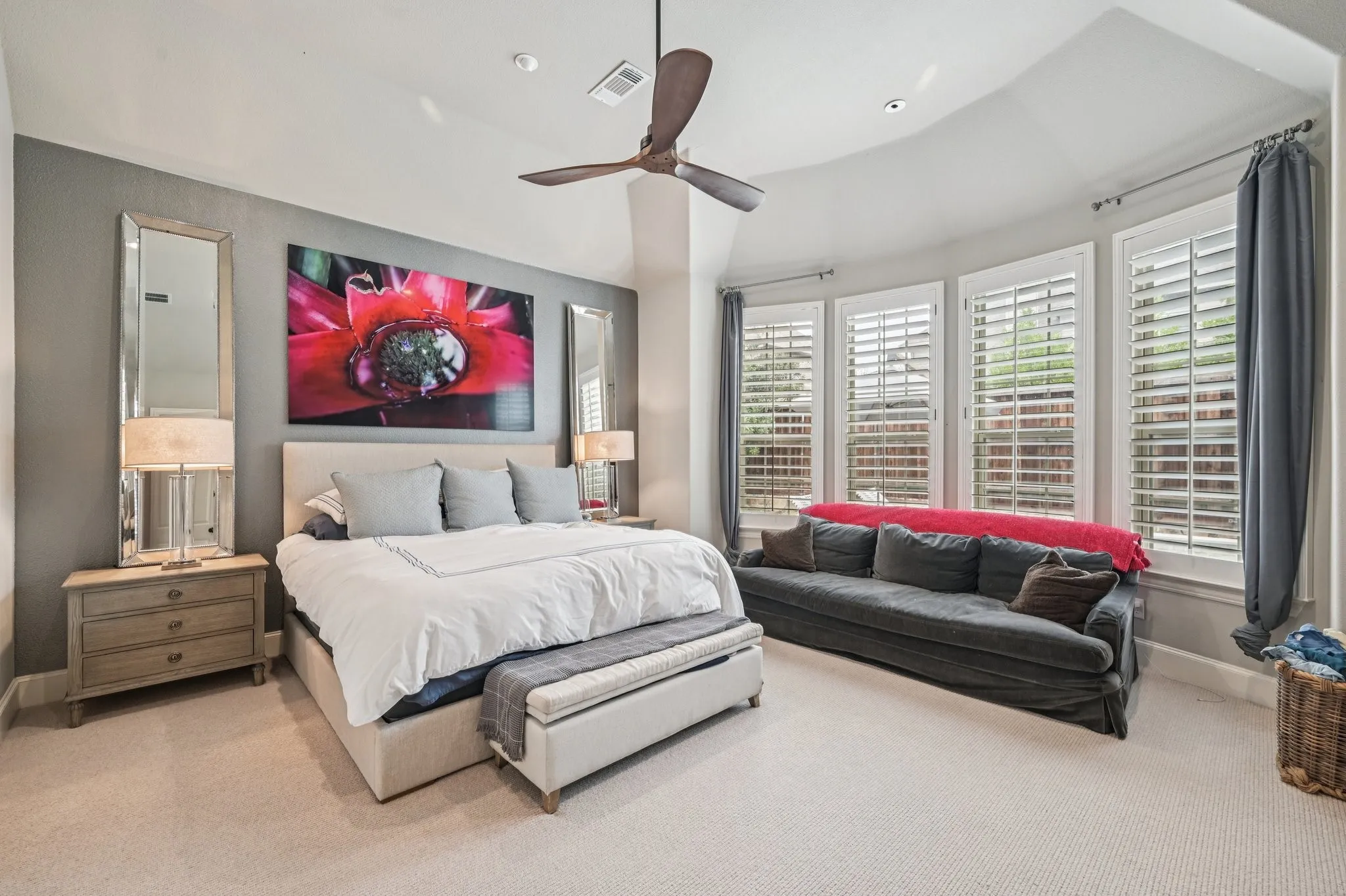 Ceiling fan with recessed lighting, bay window with plantation shutters, upholstered bed frame, and light-toned carpet flooring