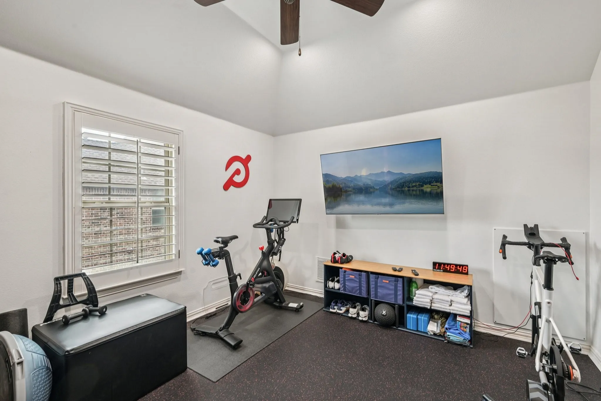 Vaulted ceiling with a ceiling fan, window with plantation shutters, wall-mounted television, and built-in shelving