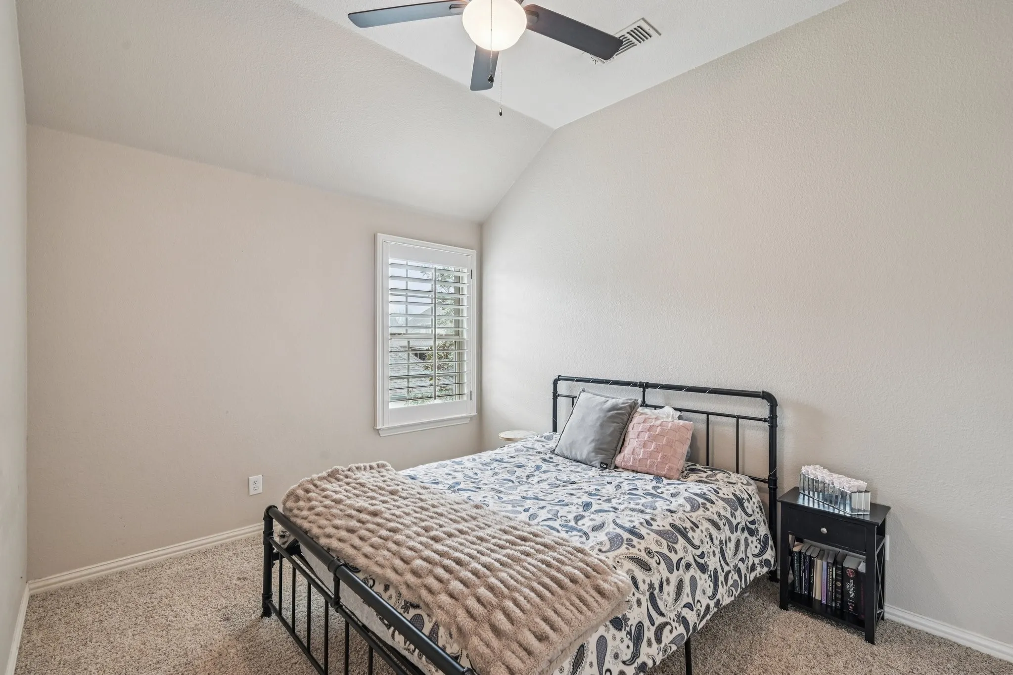 Vaulted ceiling with a ceiling fan, window with plantation shutters, and carpeting