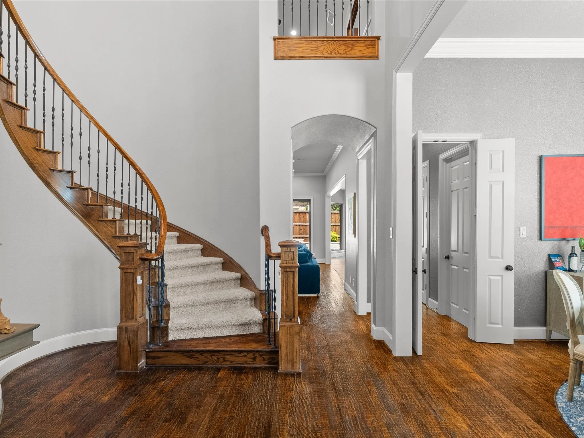 Sweeping curved staircase with wrought iron balusters and wood handrail, wood-finish flooring, arched doorway, and crown molding