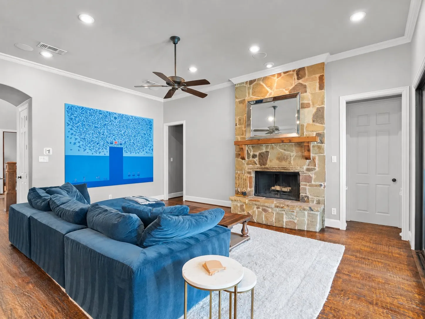 Stone-clad fireplace with wood mantel, recessed lighting, ceiling fan, crown molding, and wood-finish flooring