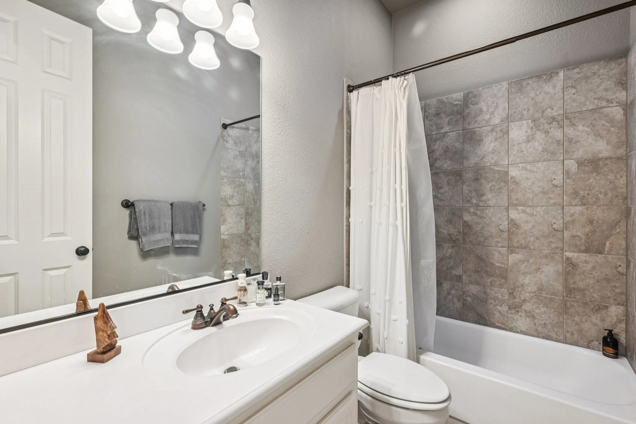 White vanity with an integrated sink, bronze-finish faucet, and a large wall-mounted mirror