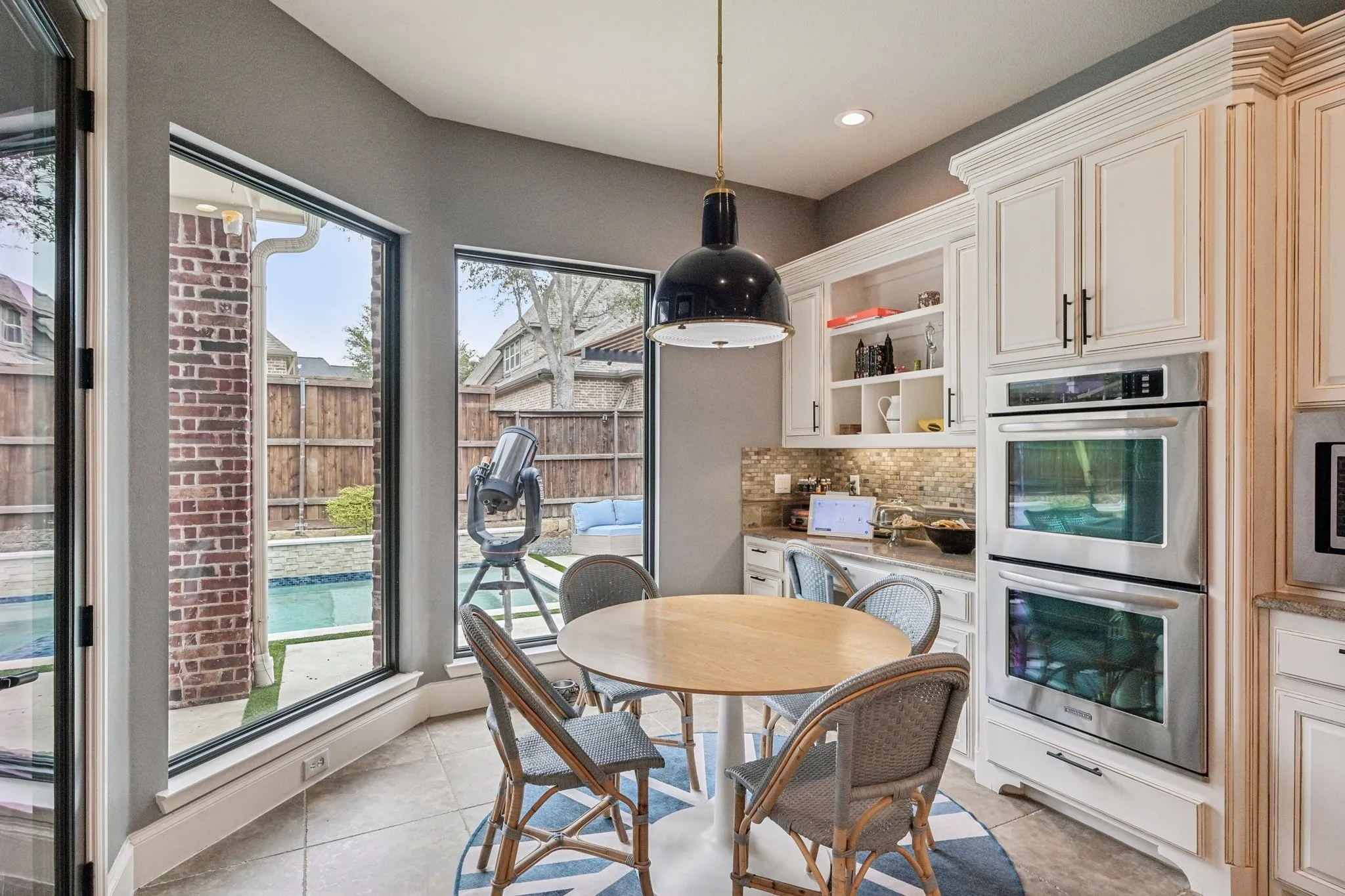 Built-in stainless steel double ovens, custom white cabinetry, and a stone backsplash complement this kitchen dining area