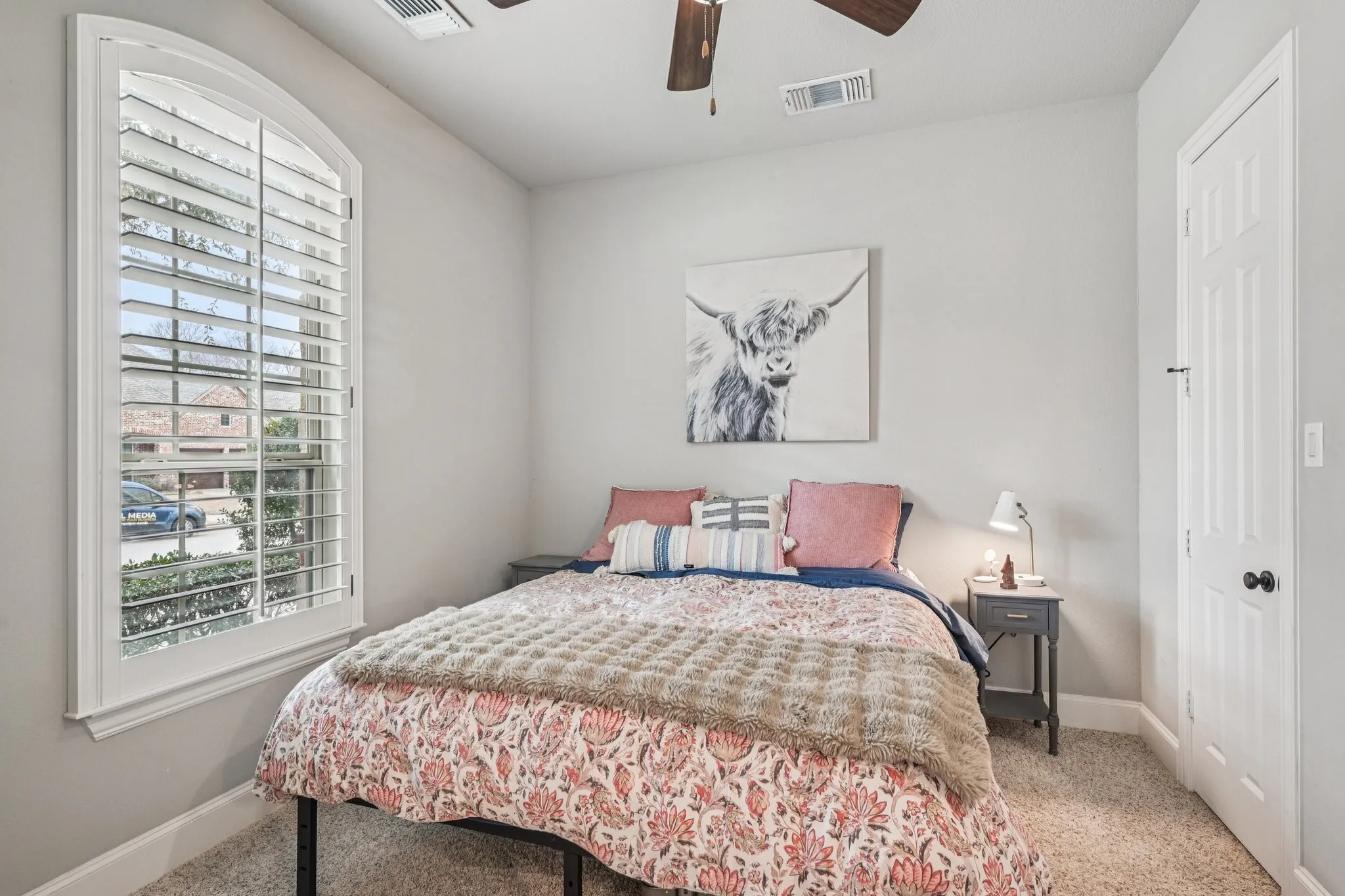Arched window with plantation shutters, ceiling fan, carpet flooring, and a paneled door