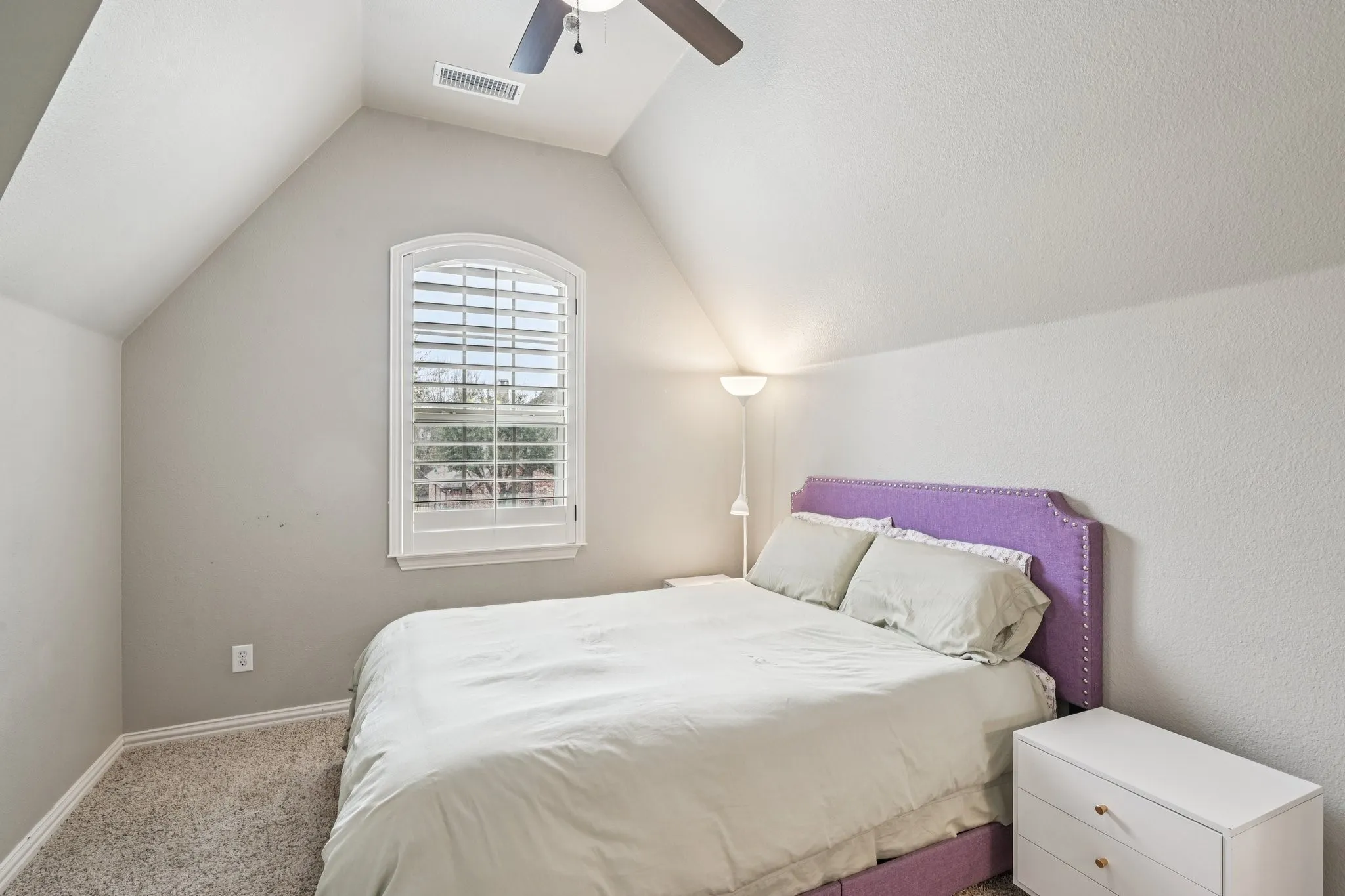Arched window with louvered shutters, sloped ceilings, textured walls, and carpet flooring