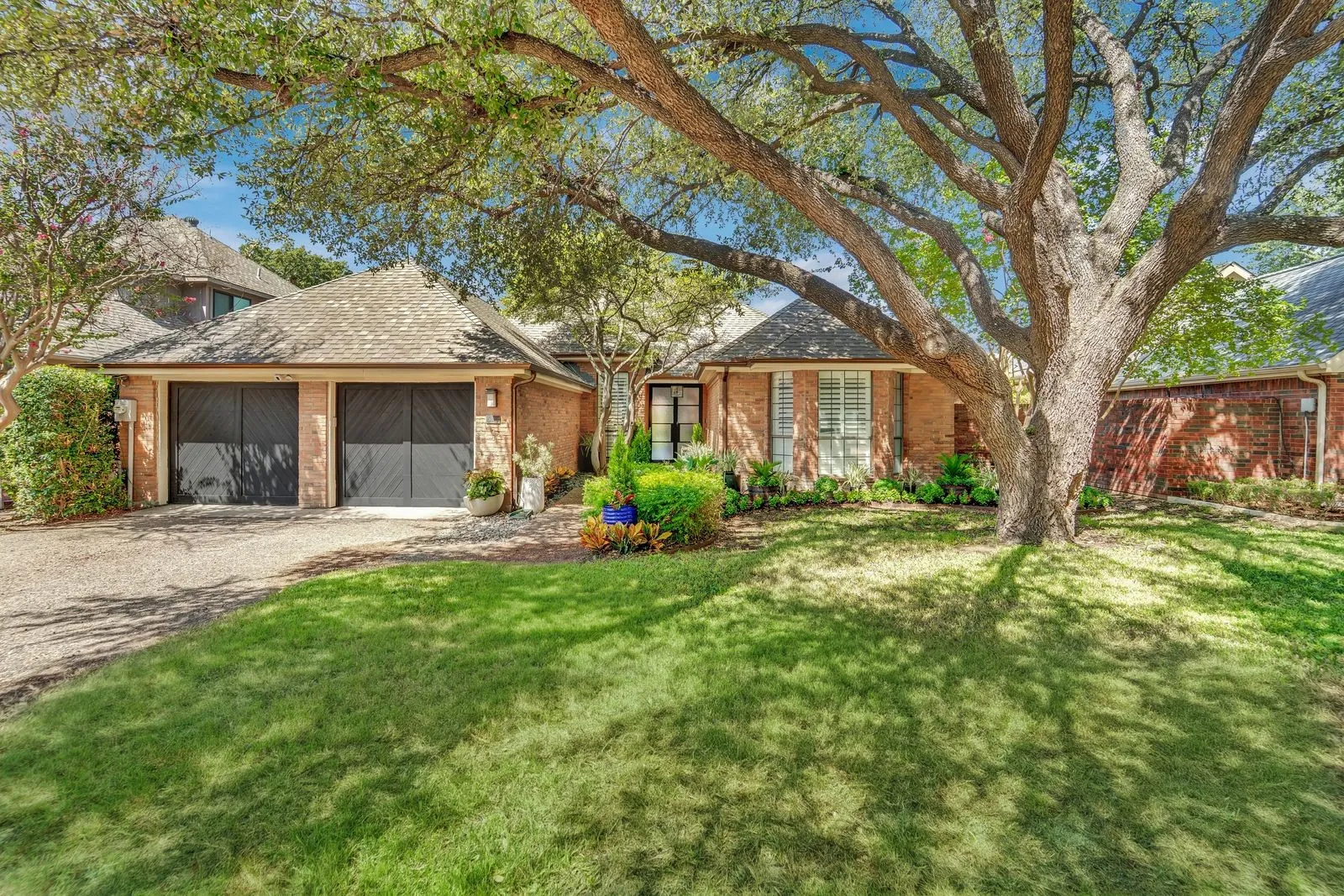 Brick exterior with a large mature tree, established landscaping, and a two-car garage