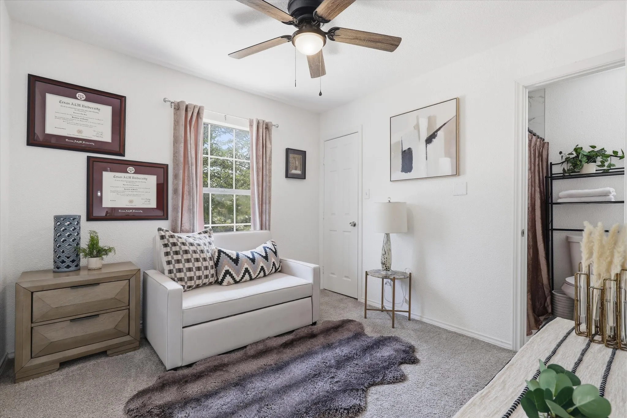 Carpeted room with a ceiling fan, a window with exterior views, and a white door leading to an adjacent bathroom with a shower curtain