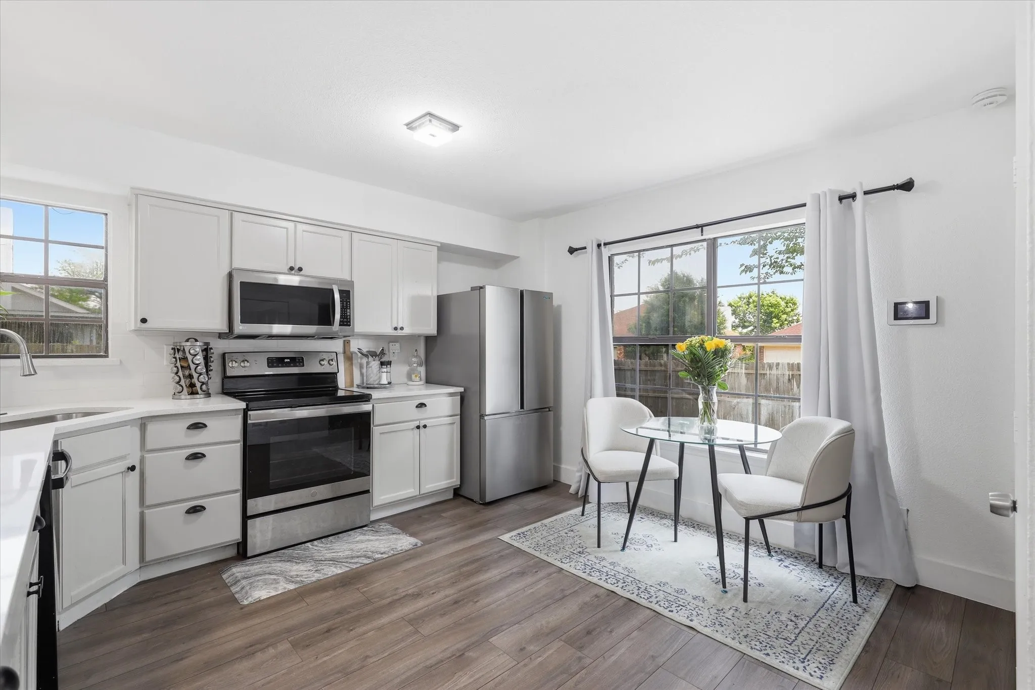 Modern kitchen featuring white cabinetry, stainless steel appliances, wood-finish flooring, and a large window