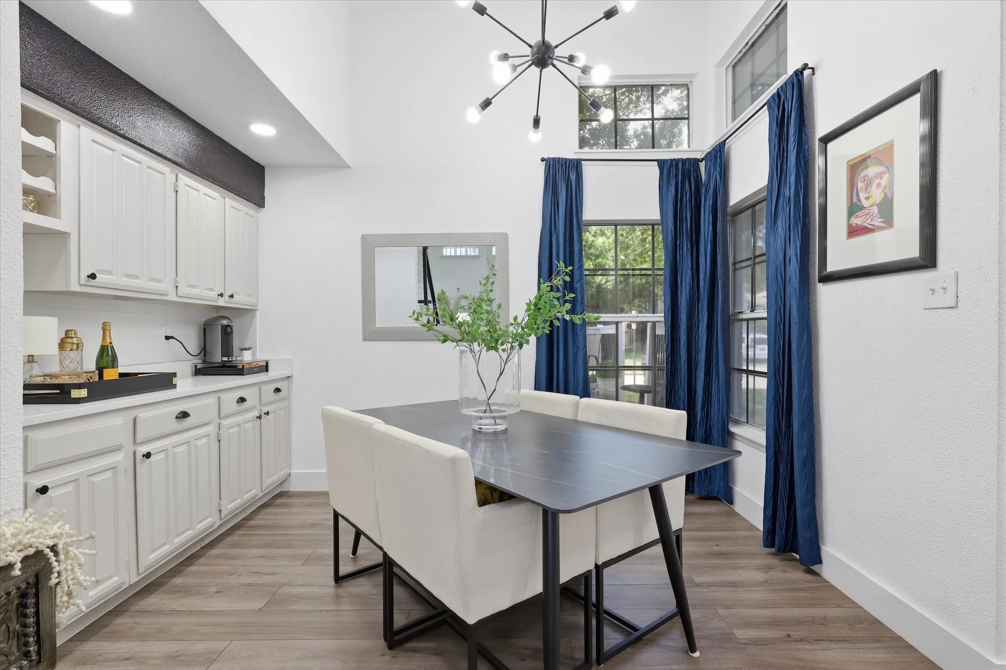 Built-in cabinetry with white shaker-style doors and black hardware, wood-finish flooring, vaulted ceilings, and a contemporary chandelier