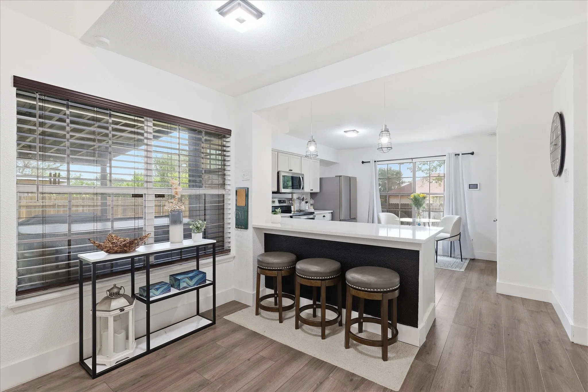 Open-concept living space with wood-finish flooring, a kitchen island with seating, pendant lighting, and a window with horizontal blinds