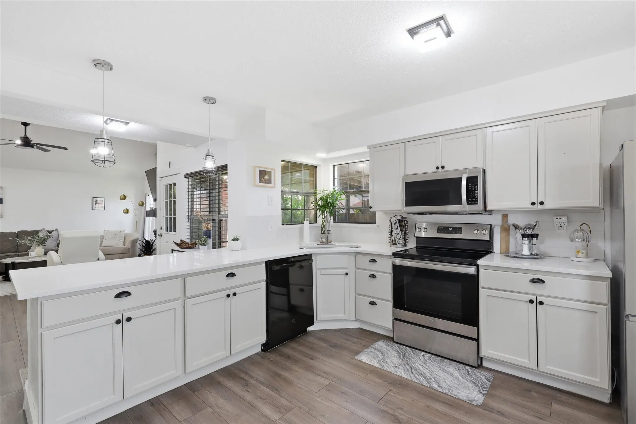 White cabinetry and countertops, wood-finish flooring, stainless steel appliances, and pendant lighting