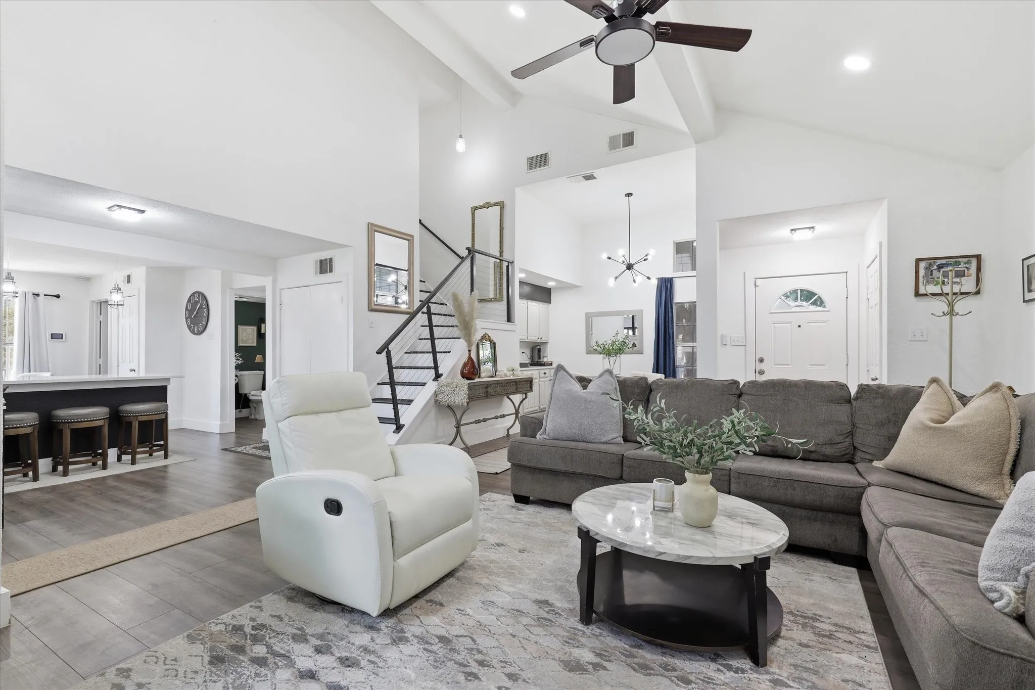 Vaulted ceilings with exposed beams, wood-finish flooring, a built-in breakfast bar, and a contemporary ceiling fan