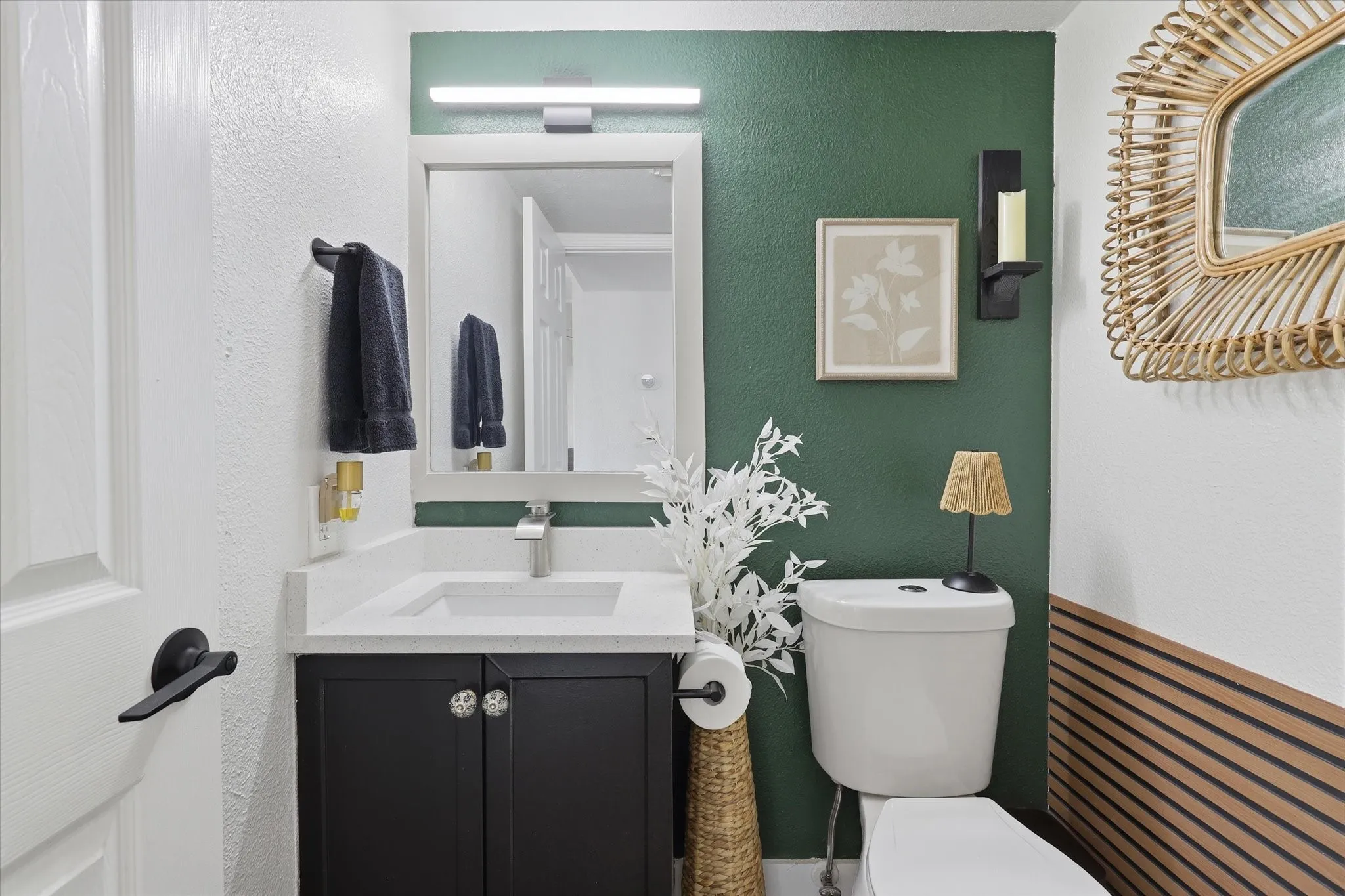 Sleek black vanity with a white countertop and integrated sink, complemented by a mirror with a wall-mounted light fixture