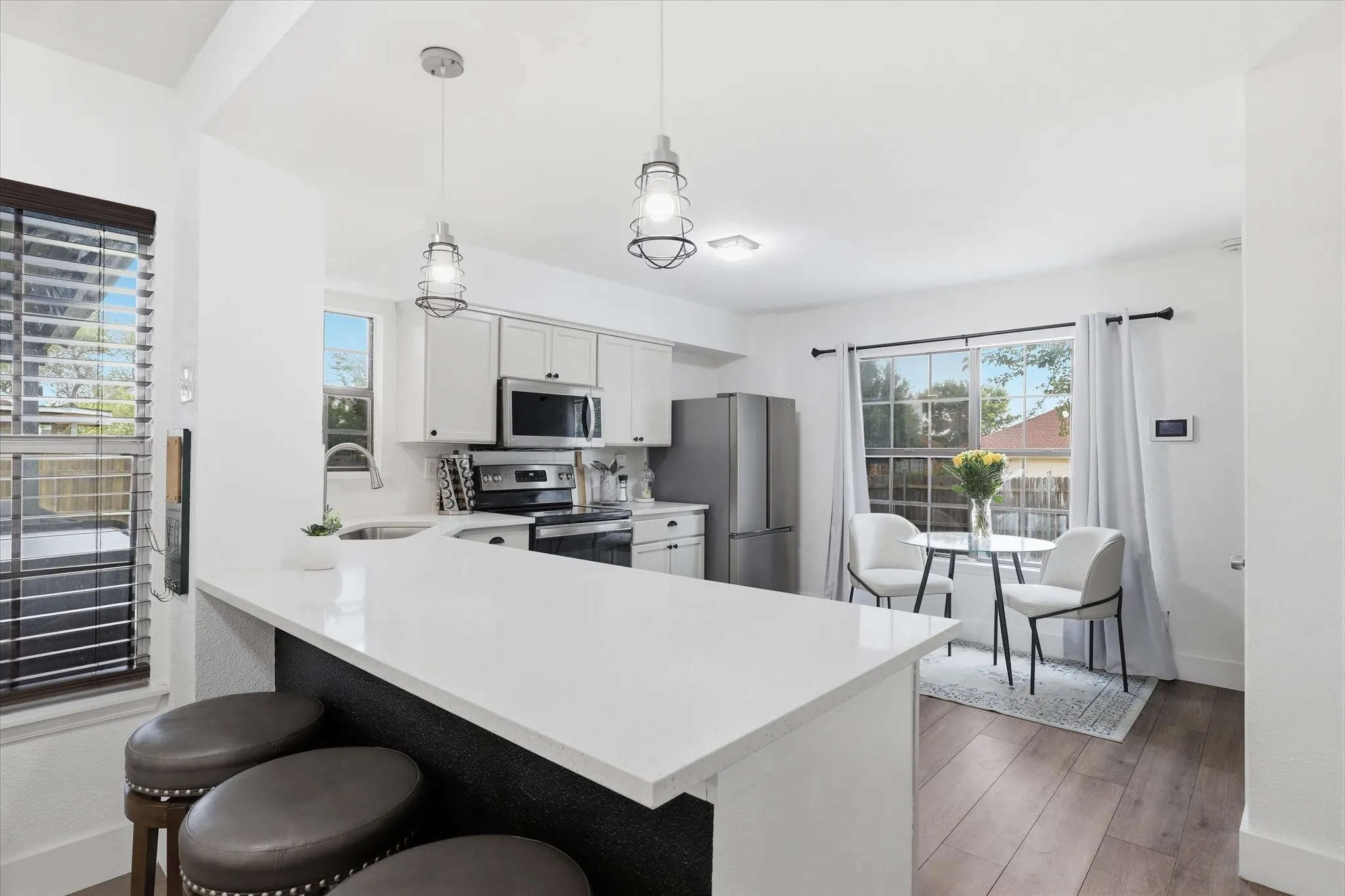 Kitchen featuring white shaker cabinetry, stainless steel appliances, a white island countertop, and wood-finish flooring