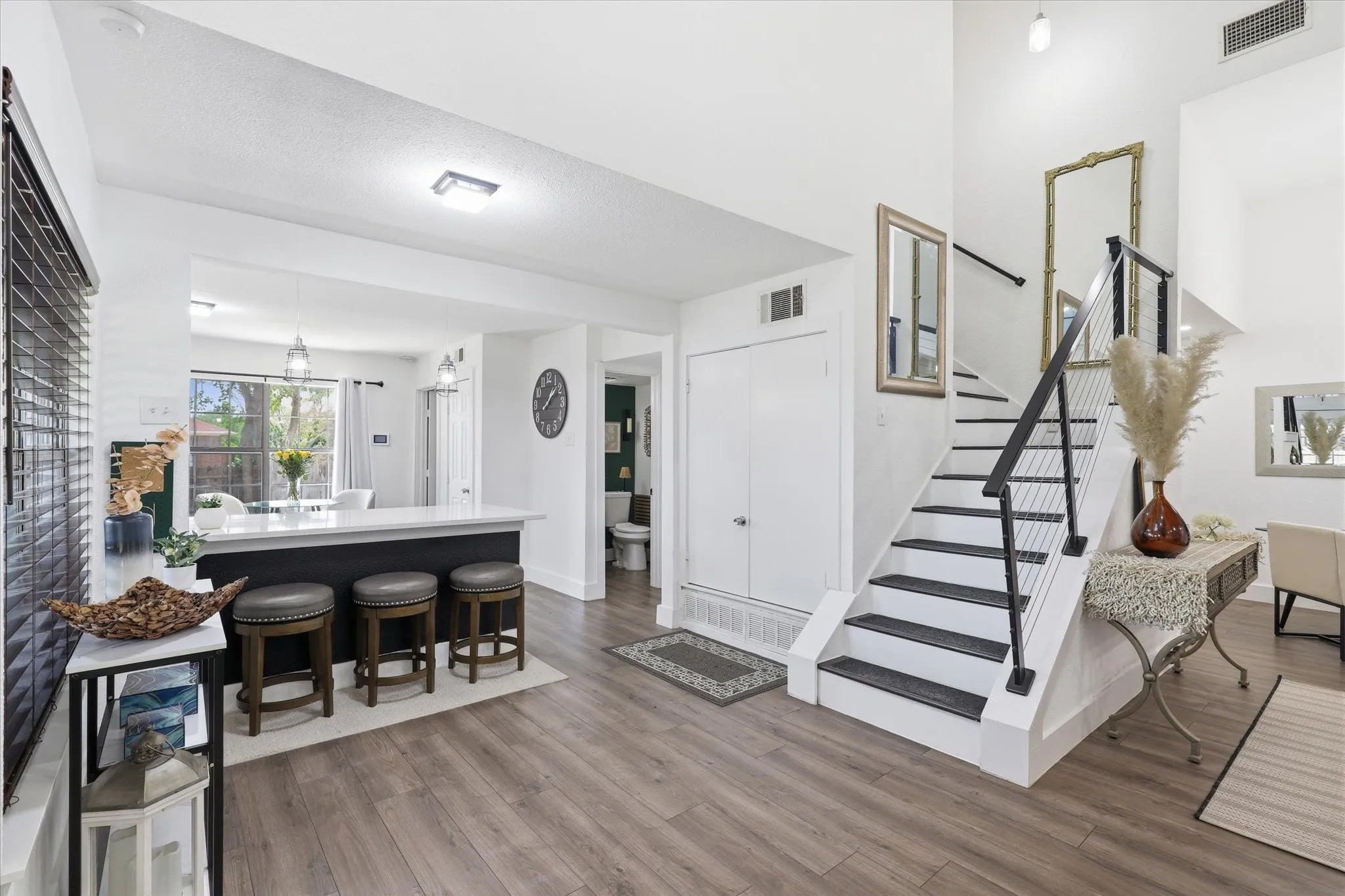 Wood-finish flooring throughout, an open-concept kitchen island with pendant lighting, a two-story entryway with a modern staircase, and a built-in storage closet