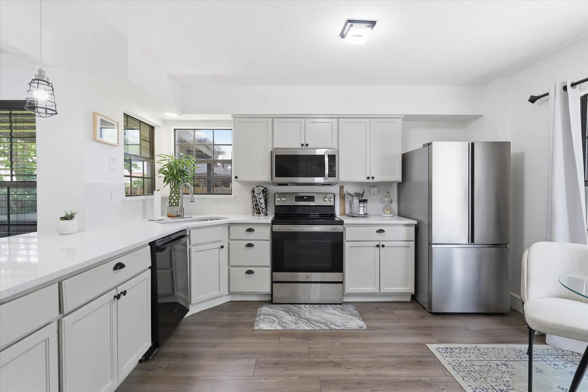 White shaker cabinetry, stainless steel appliances, white countertops, wood-finish flooring, and a single basin sink