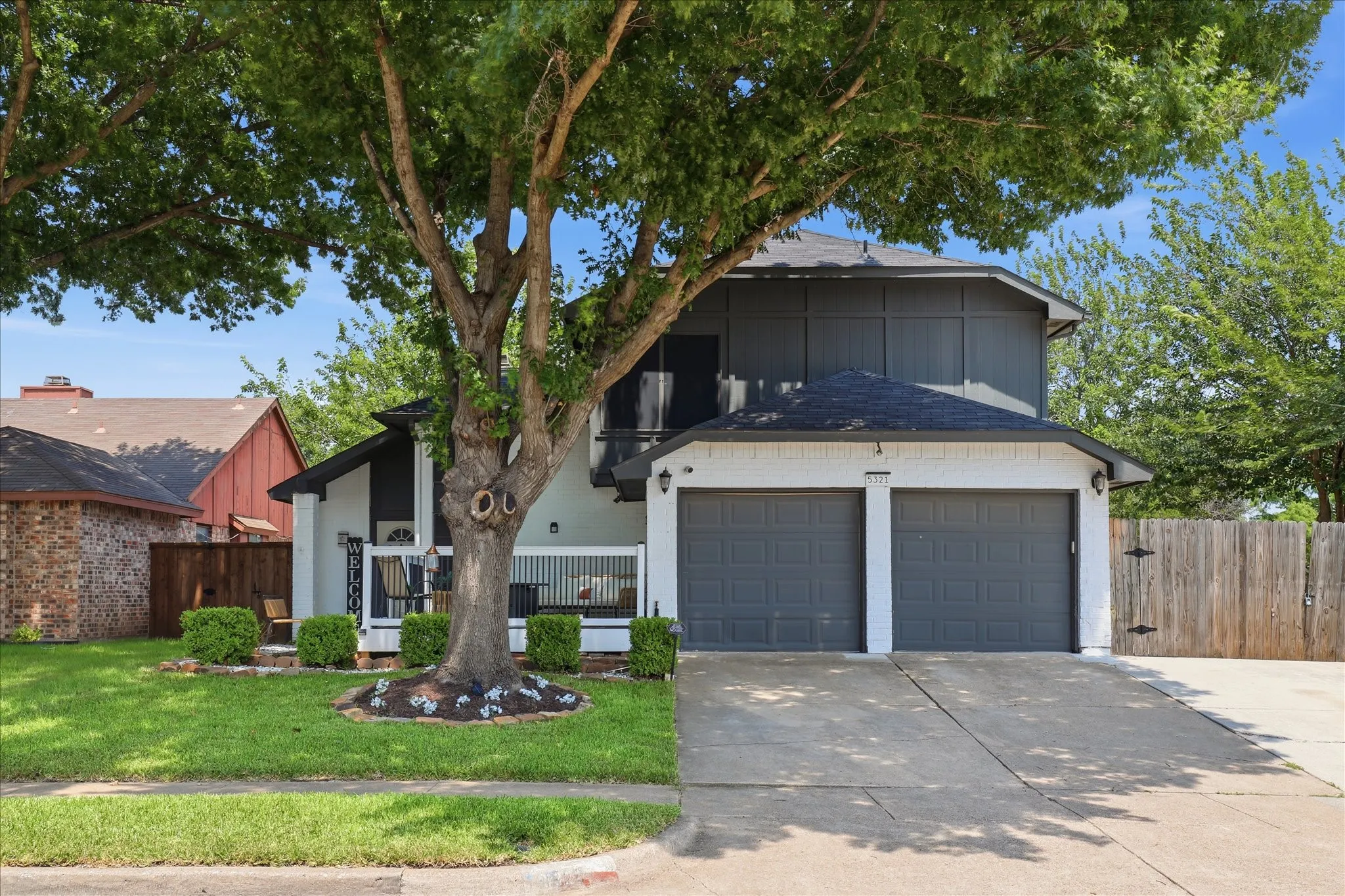 Two-story residence with a two-car garage, established front yard landscaping, and mature trees