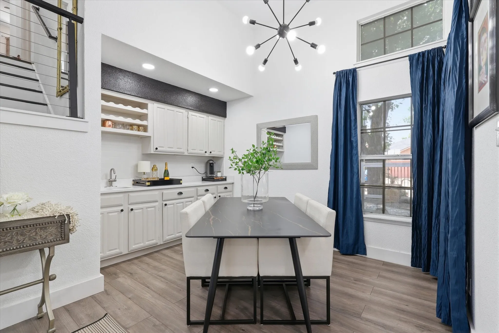 Vaulted ceiling with a contemporary chandelier, built-in wet bar with white cabinetry and integrated wine storage, wood-finish flooring, and large windows