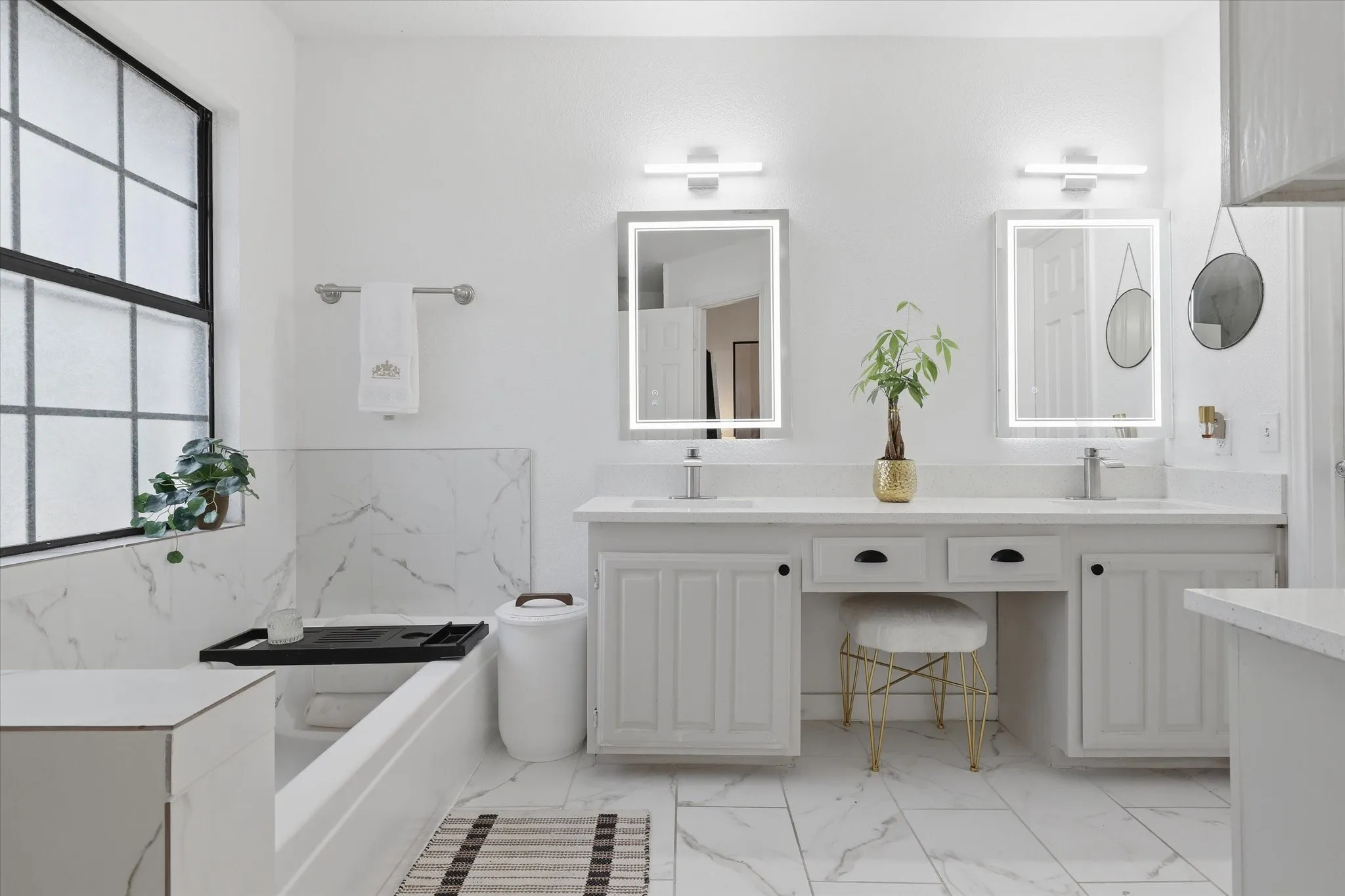 Dual vanity with integrated sinks, illuminated mirrors, built-in cabinetry, large soaking tub, and tile flooring